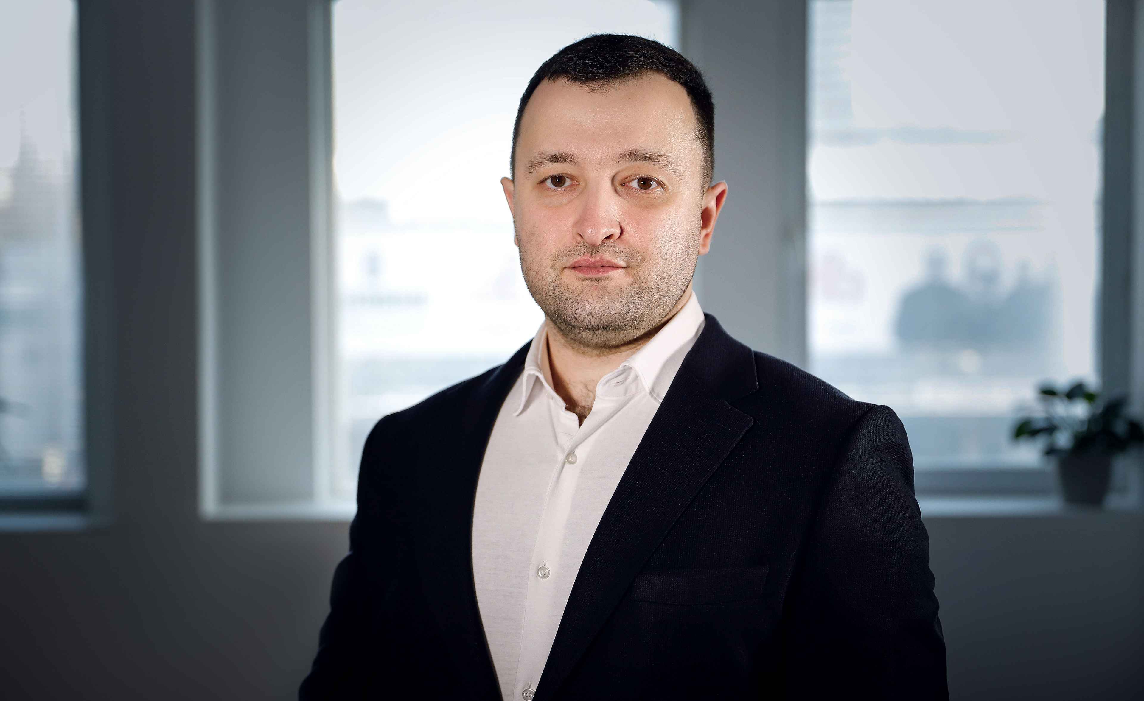 Чоловік в чорному піджаку і білій сорочці стоїть на фоні вікна. Це Василенко Володимир Андрійович, Заступник Міністра соціальної політики України