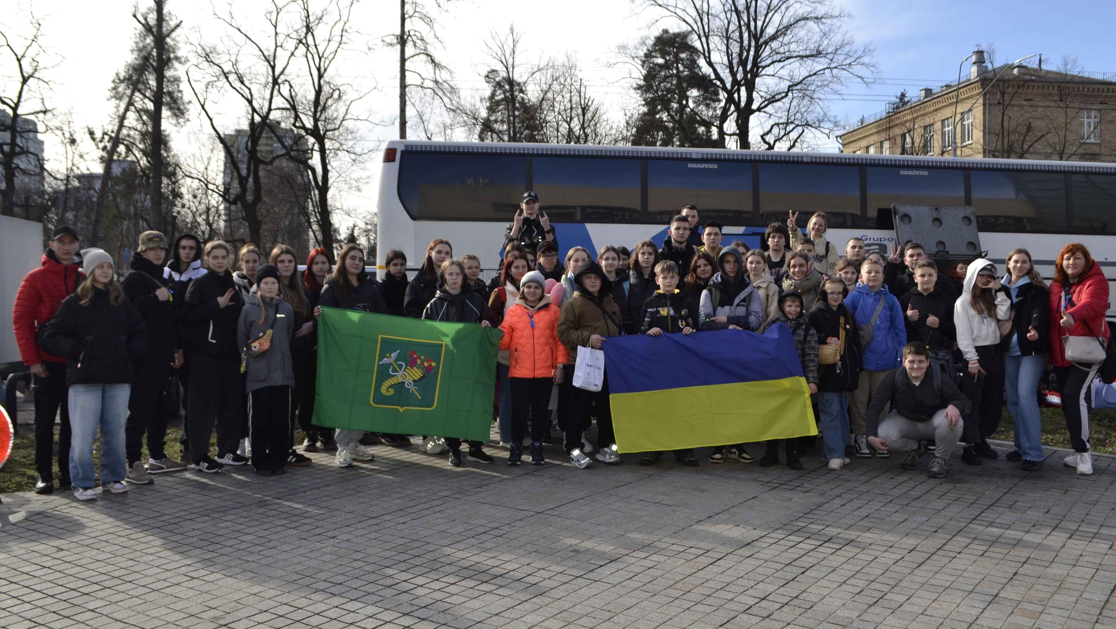 Діти з прапорами на фоні автобуса