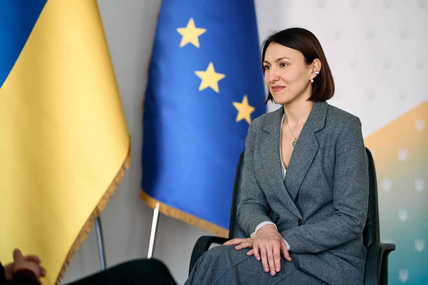 На фото заступниця Міністра соціальної політики, сім'ї та єдності України з питань європейської інтеграції Ілона Гавронська сидить на фоні прапорів України та ЄС