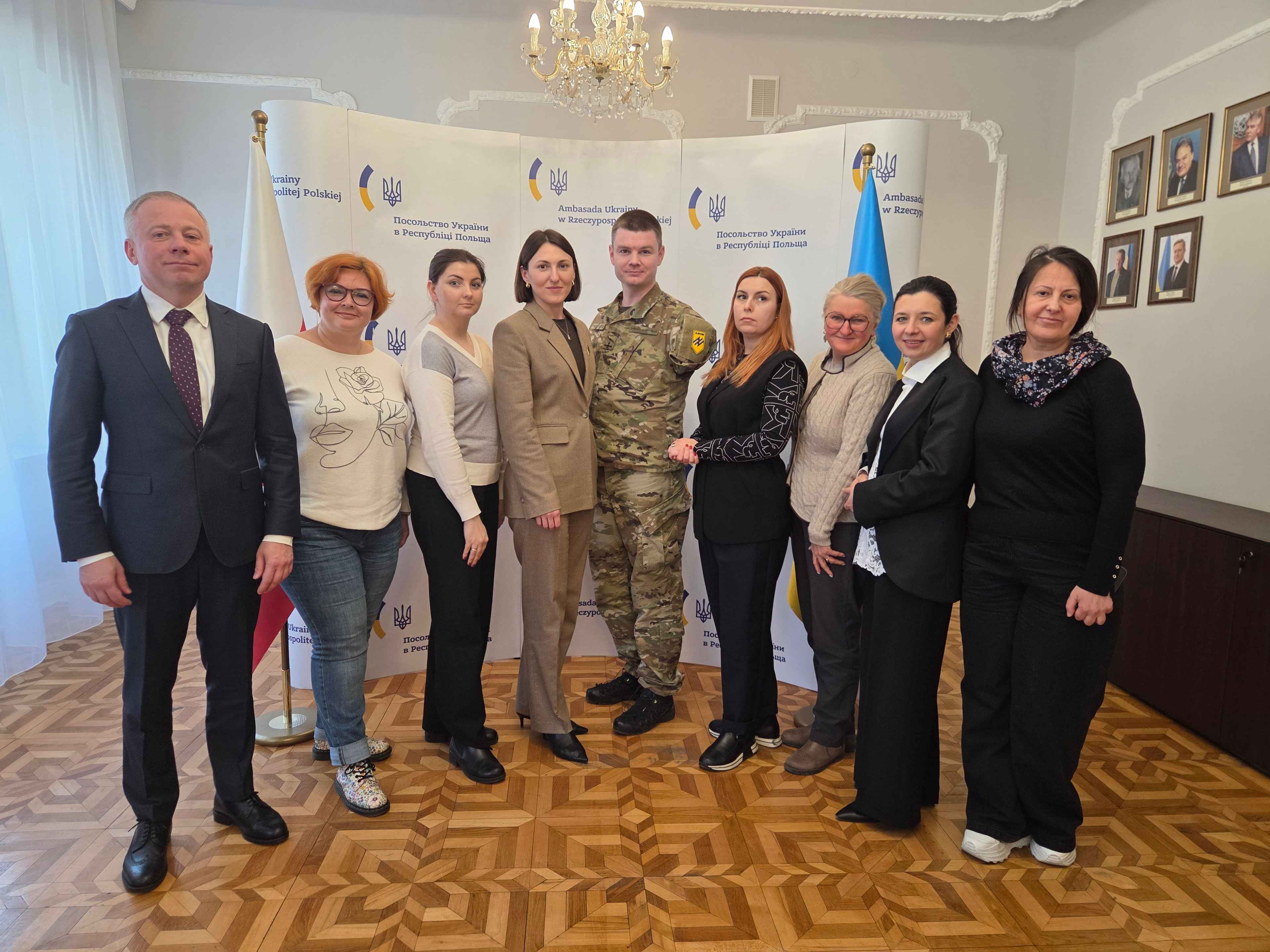 На фото жінки та чоловіки стоять на фоні банеру