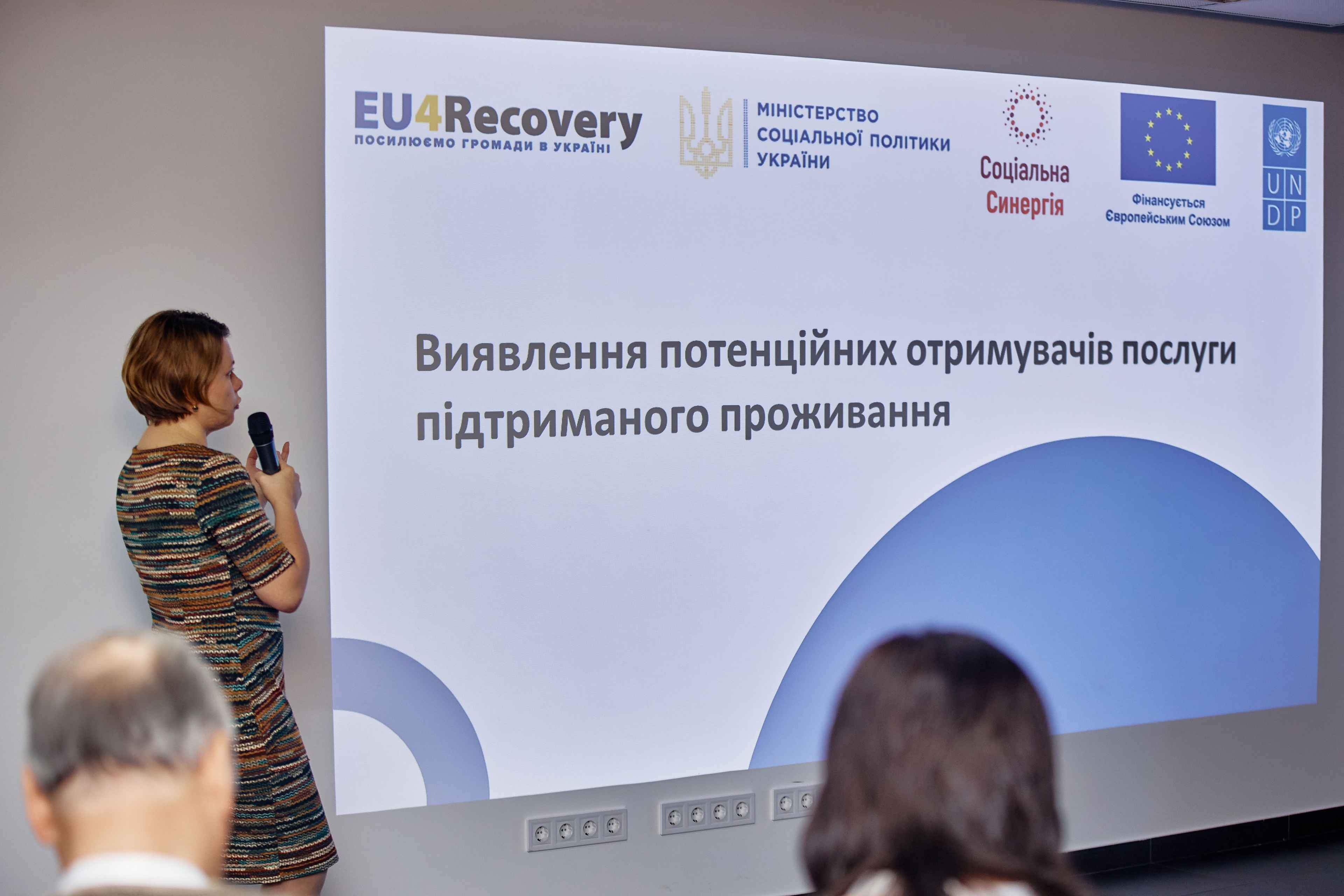 На фото зображена на жінка на фоні банеру "Виявлення потенційних отримувачів послуг підтриманого проживання"