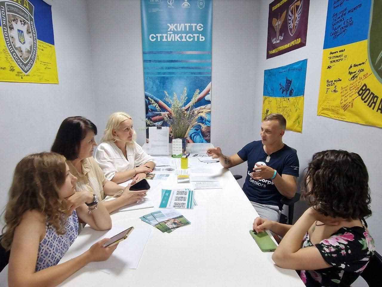 На фото чловік та жінки сидять за столом у Центрі життєстійкості і спілкуються