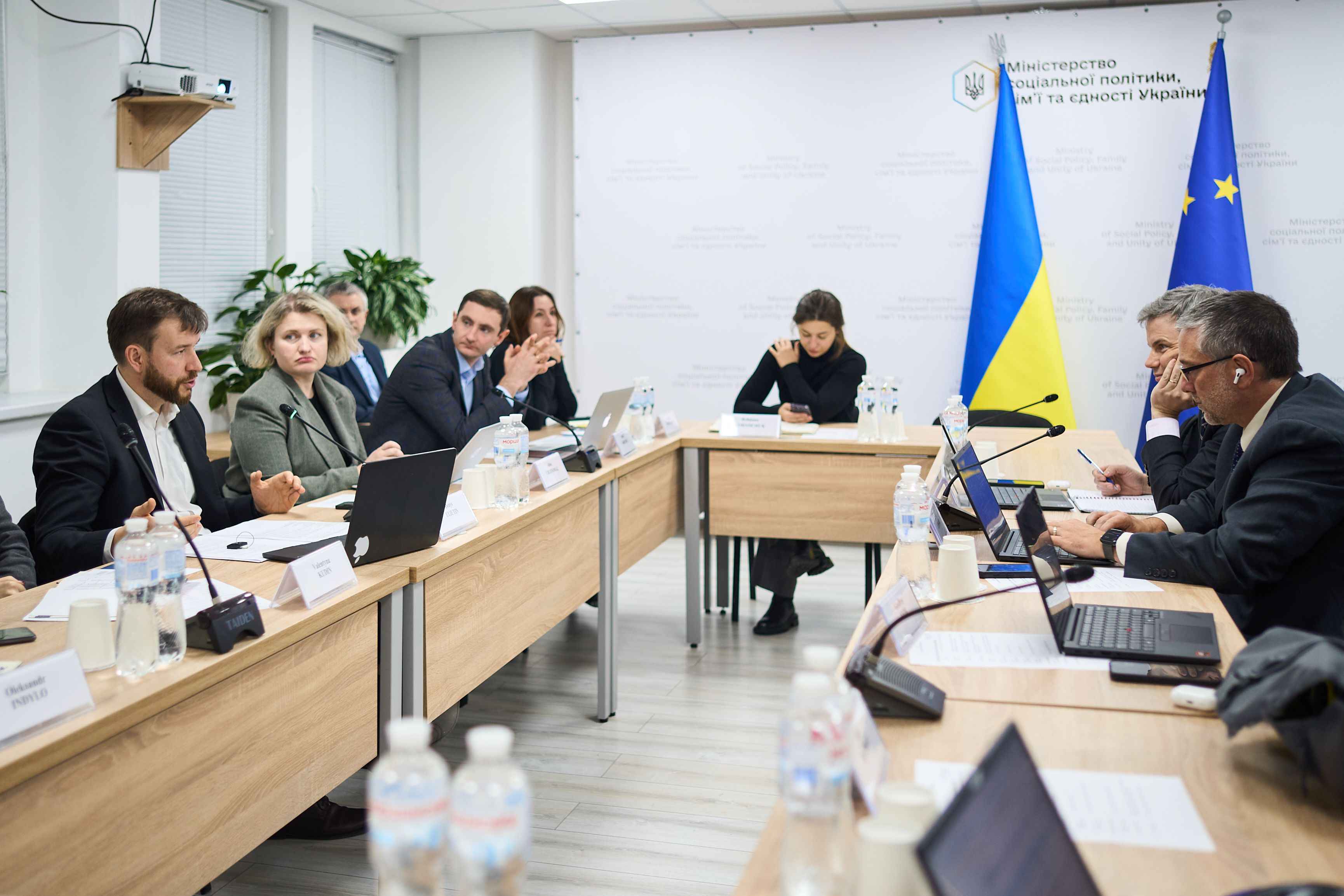 На фото чоловіки та жінки сидять за столом під час зустрічі