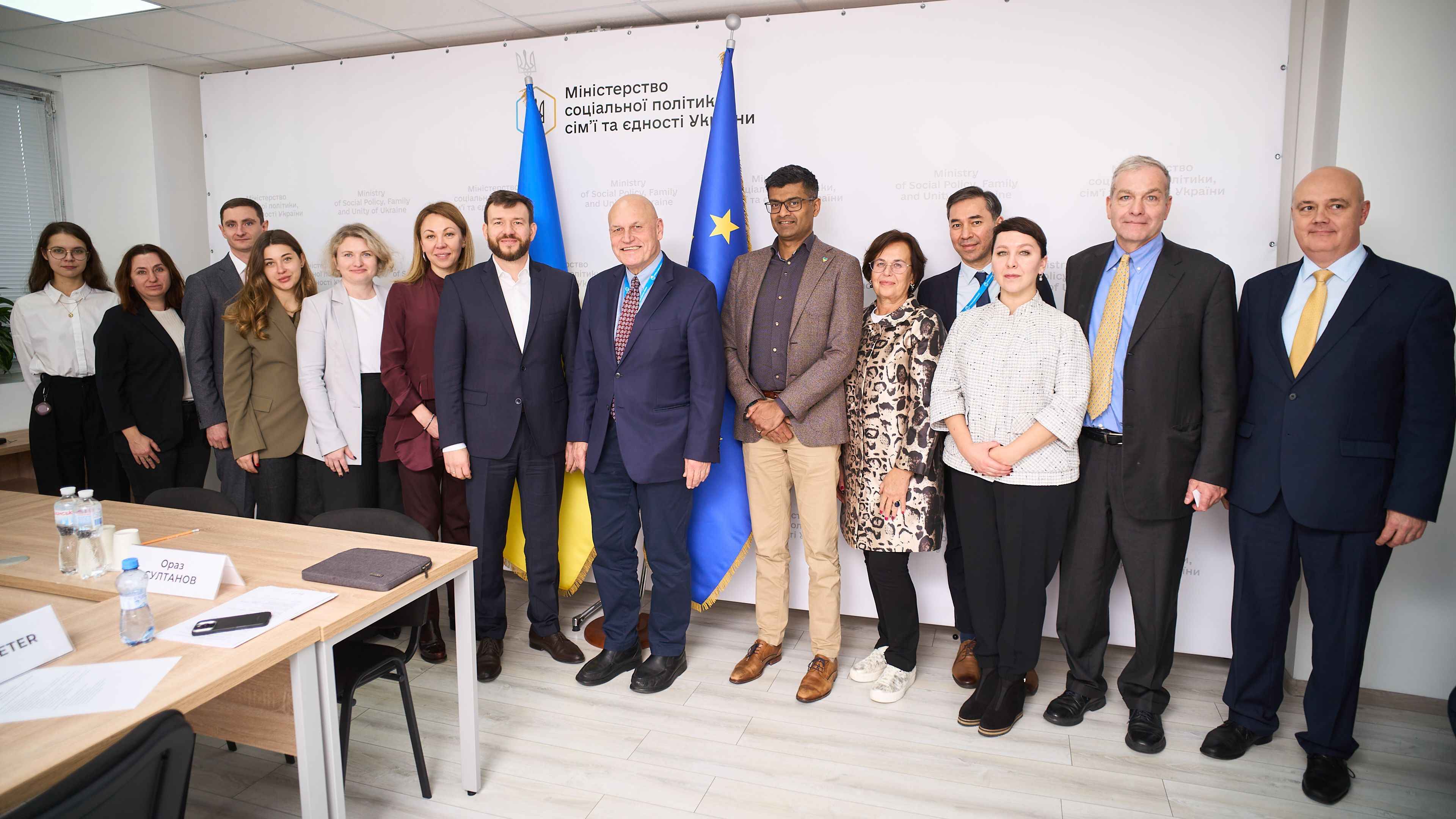 На фото чоловіки та жінки стоять після зустрічі на фоні прапорів України та ЄС