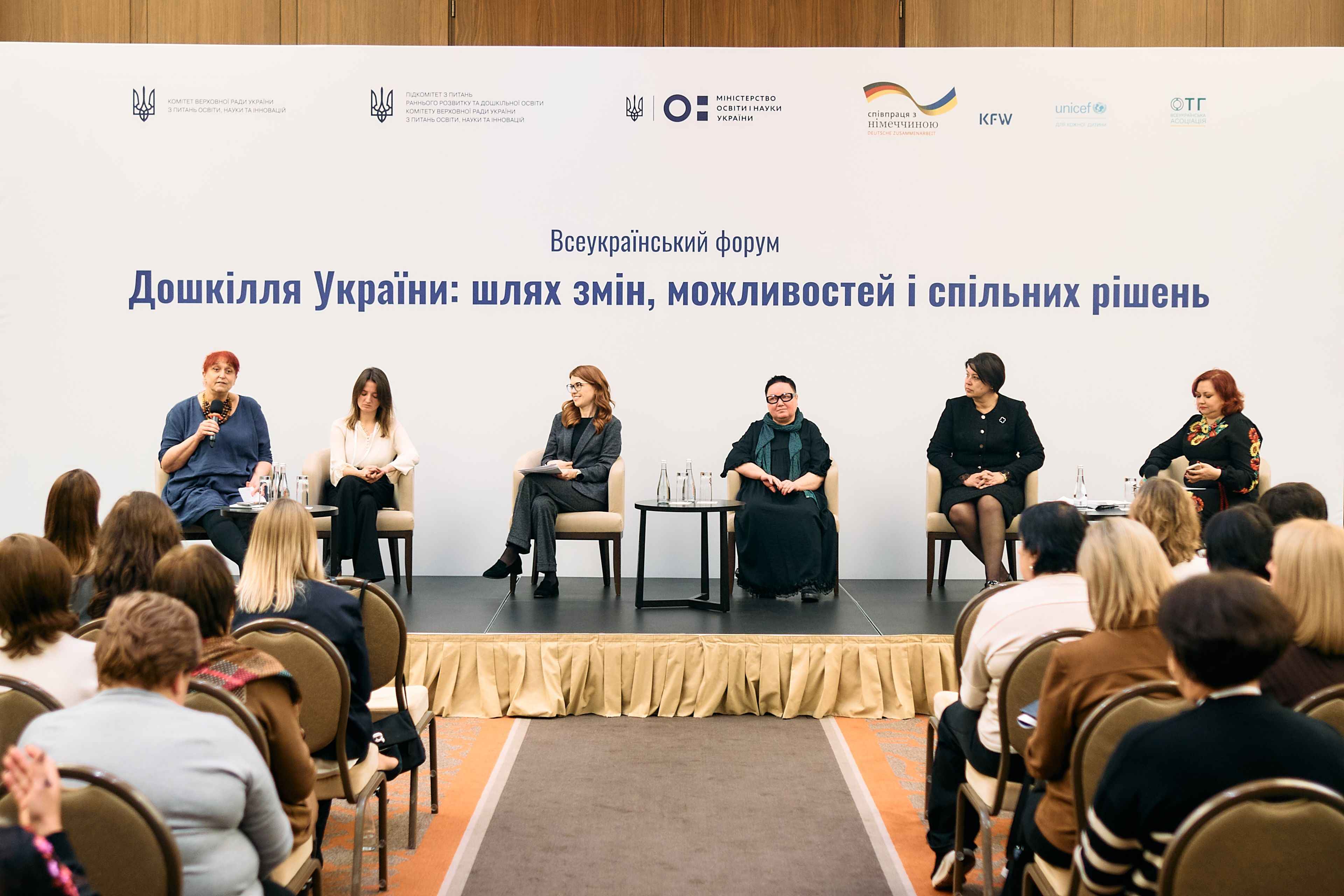 На фото жінки та чоловіки сидять у президії під час заходу