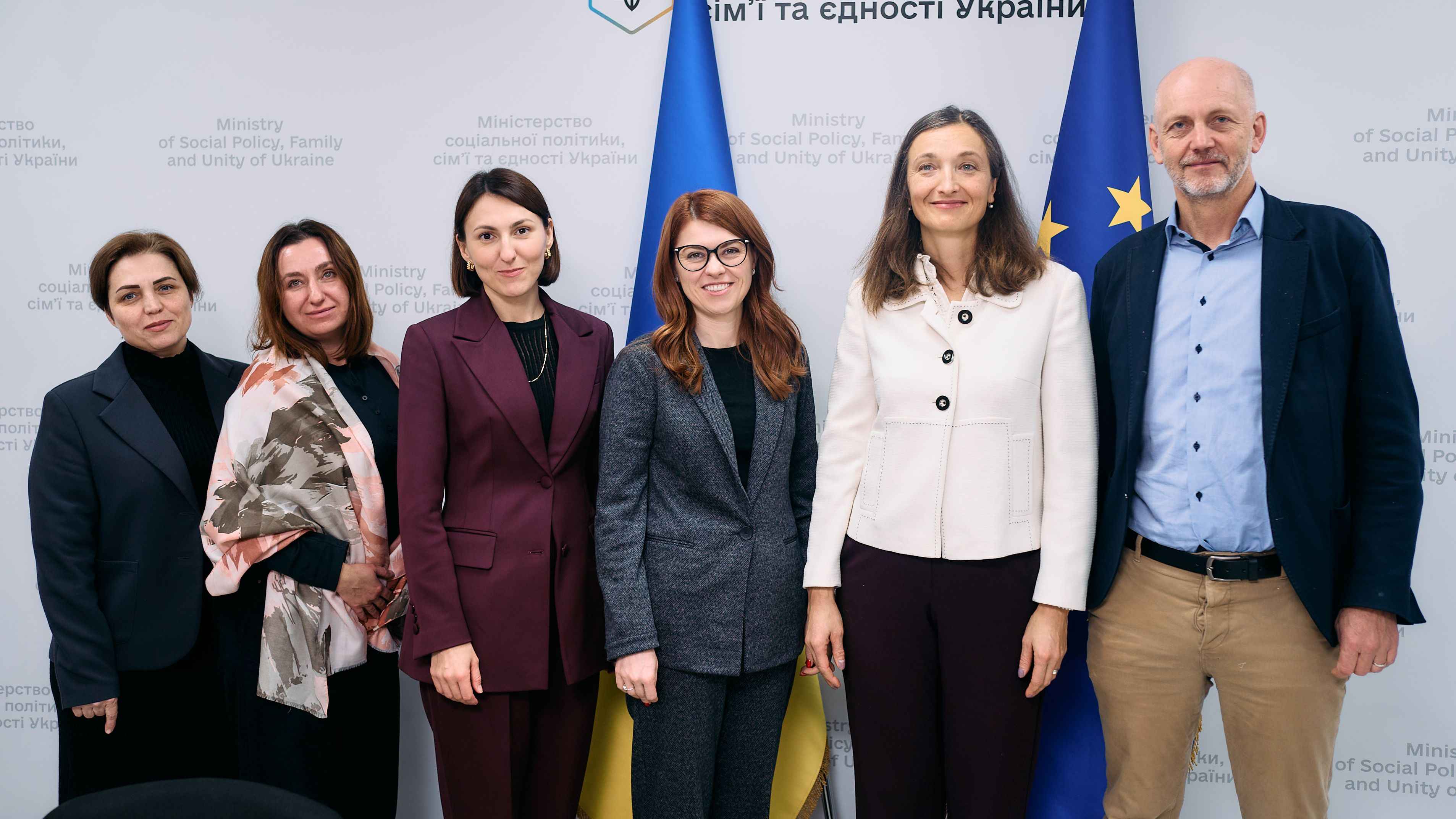 На фото жінки та чоловік стоять на фоні прапорів України та ЄС після зустрічі