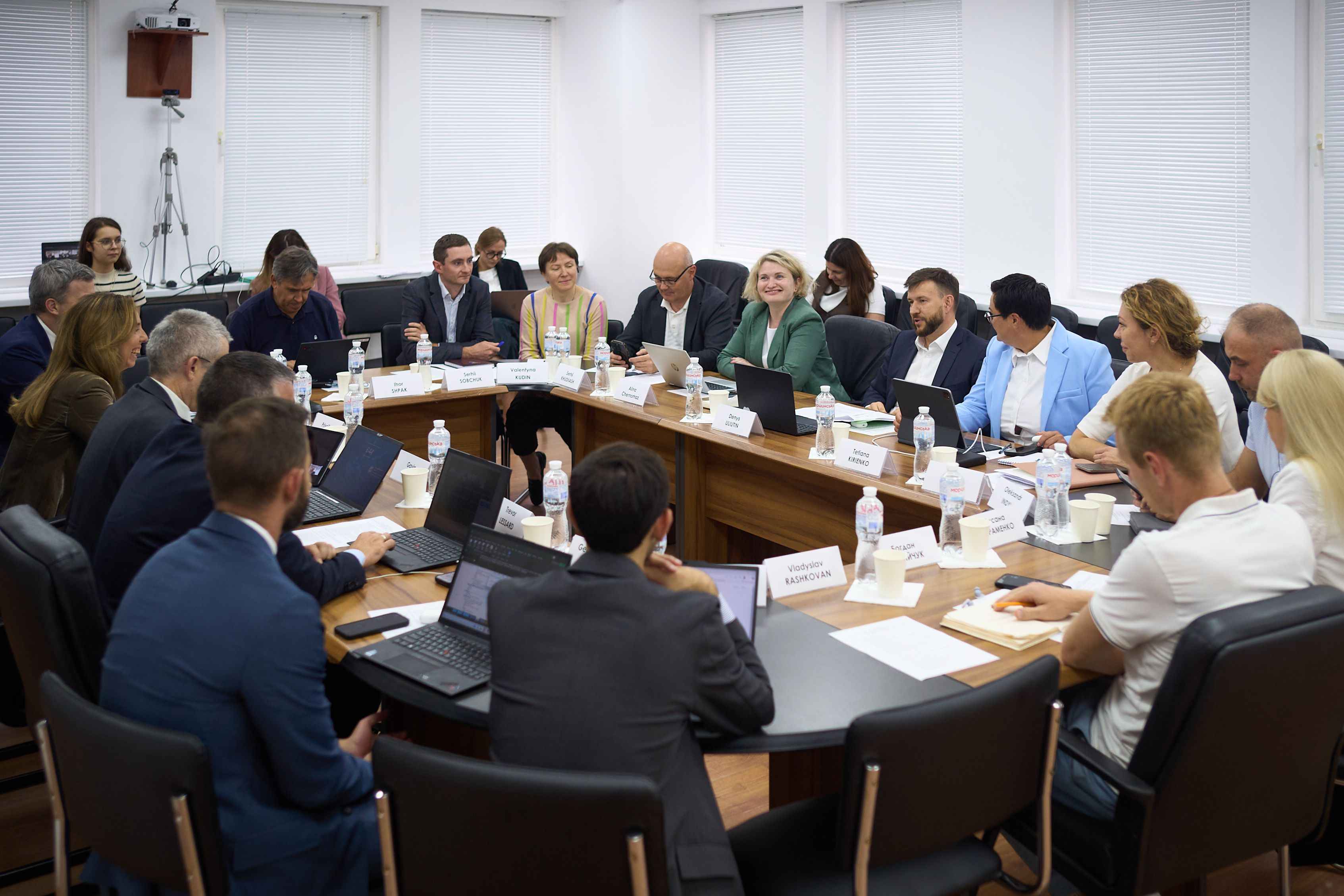 На фото зображено чоловіків та жінок. які сидять за столом під час зустрічі