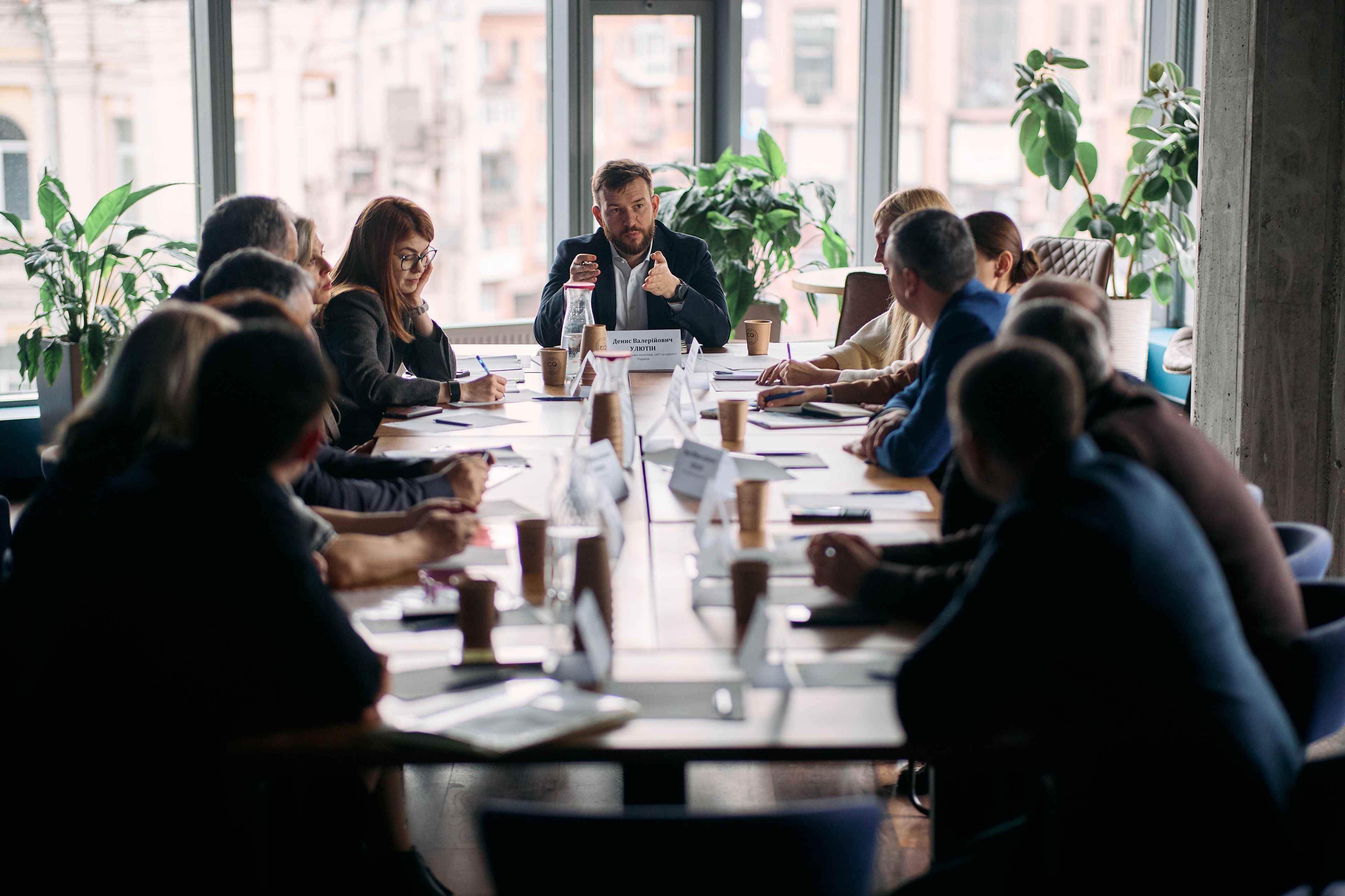На фото чоловіки та жінки сидять за столом під час заходу