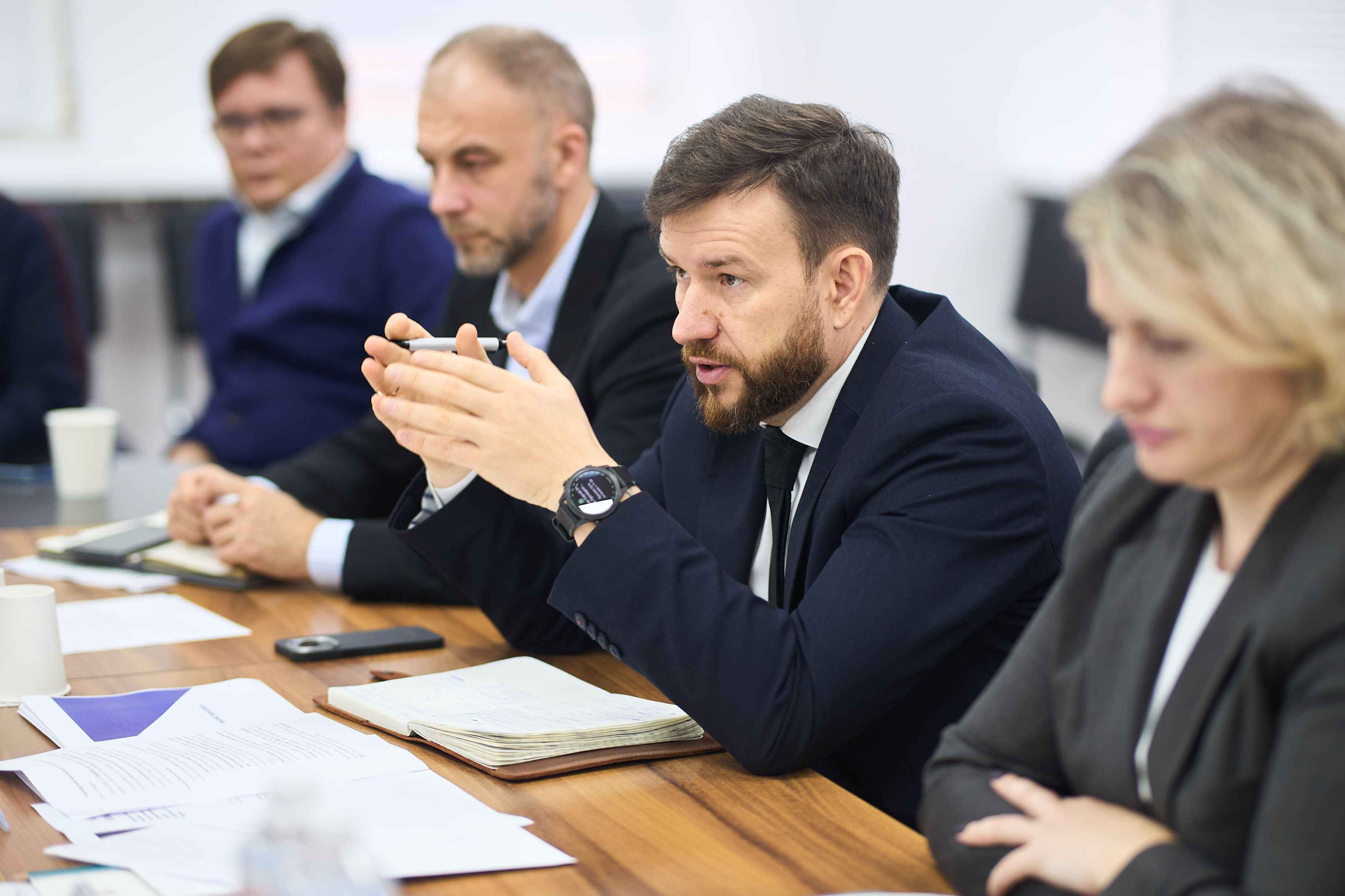 На фото чоловіки та жінка сидять за столом під час зустрічі