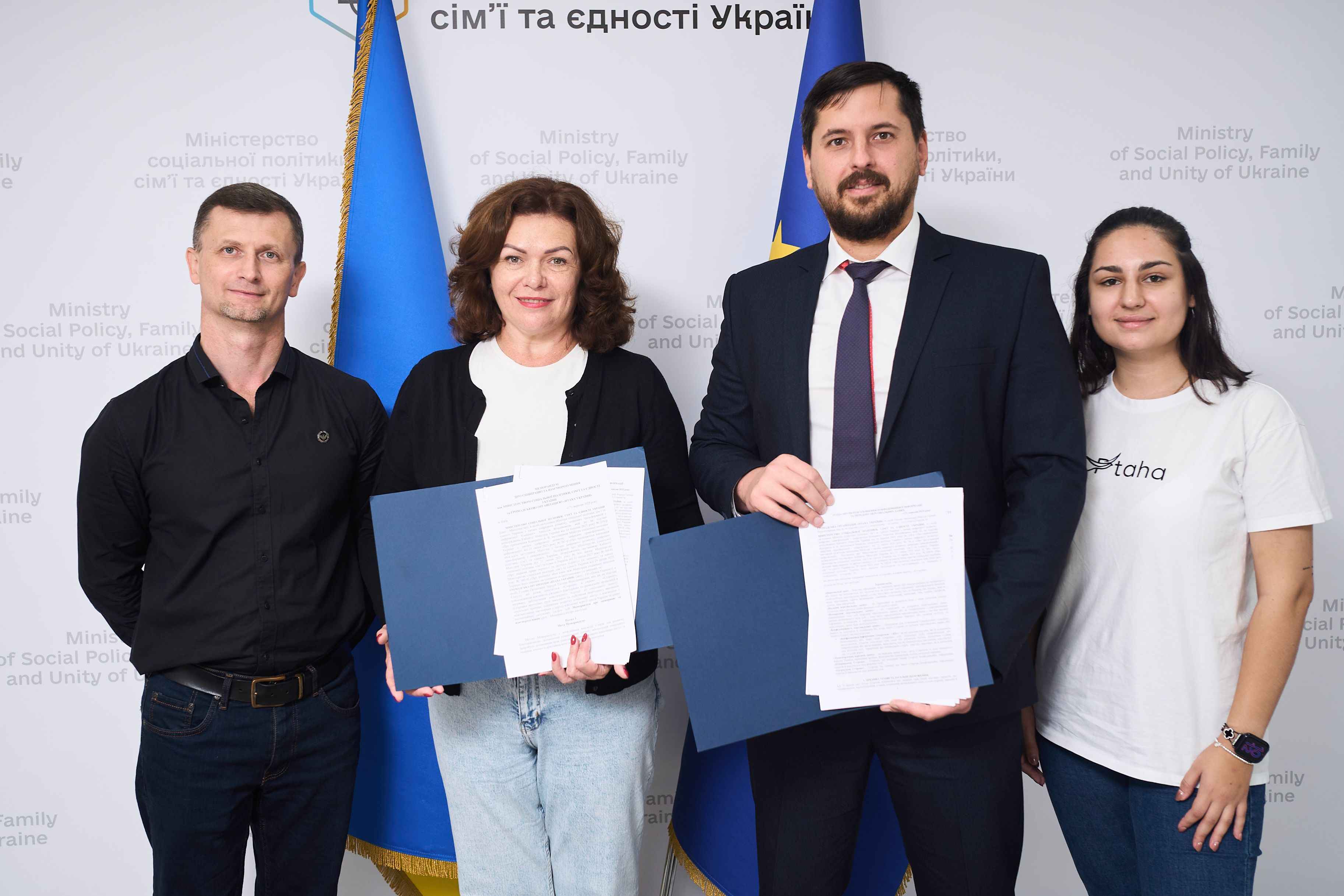 На фото зображено жінки та чоловіки, які стоять на фоні прапорів України та ЄС