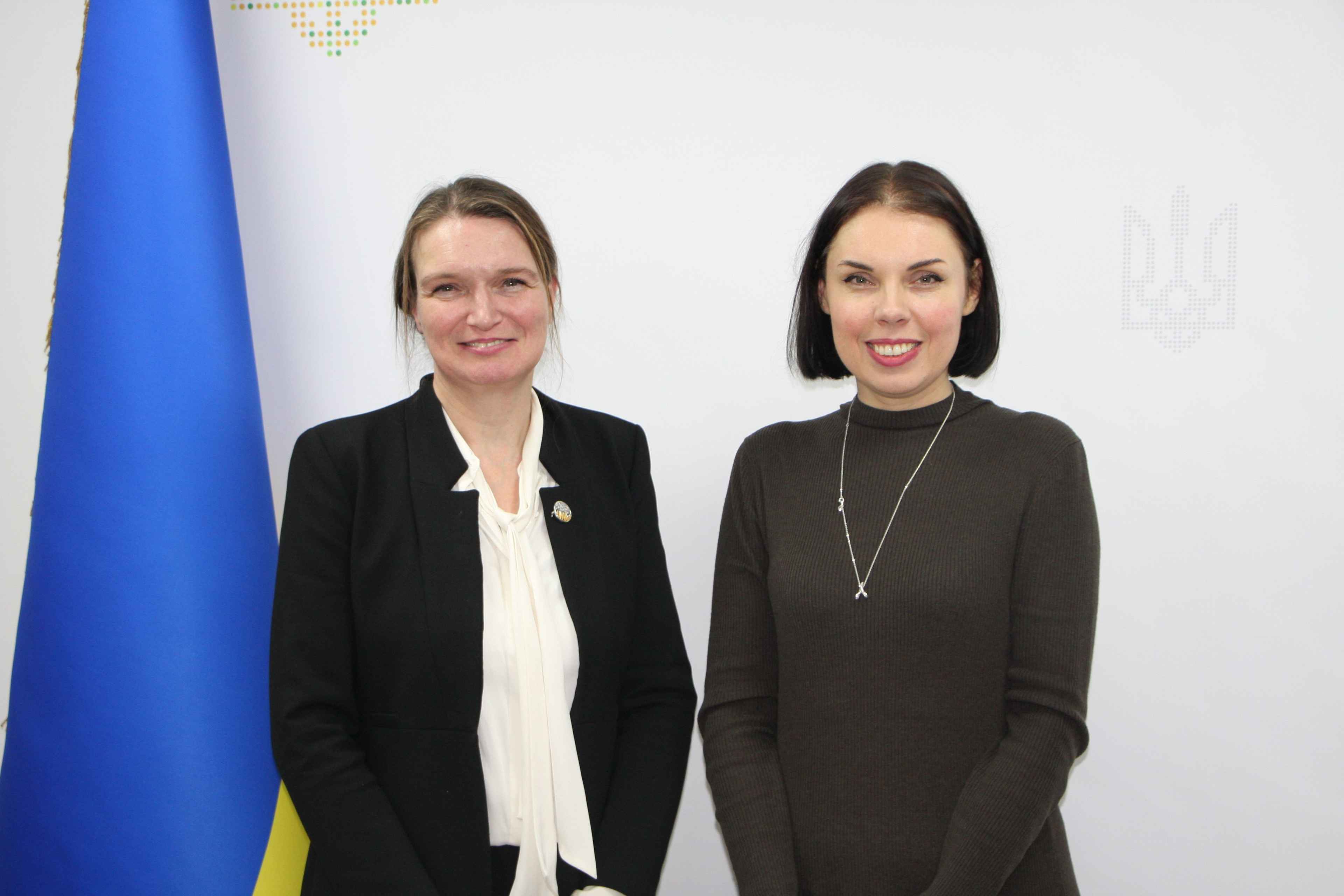 Двоє жіно стоять на фоні жовто-блакитного прапору
