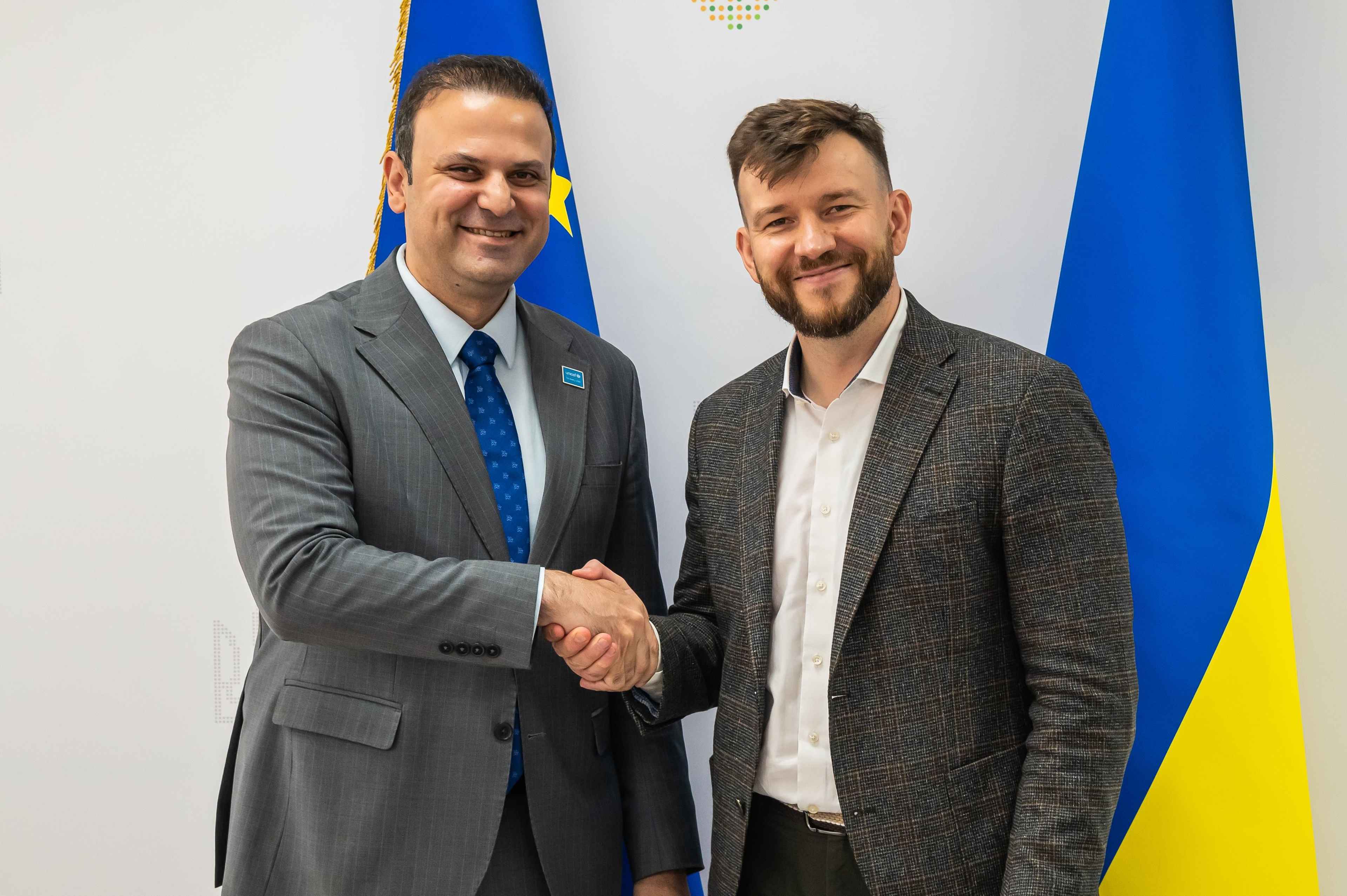 На фото двоє чоловіків стоять на фоні прапорів ЄС та України