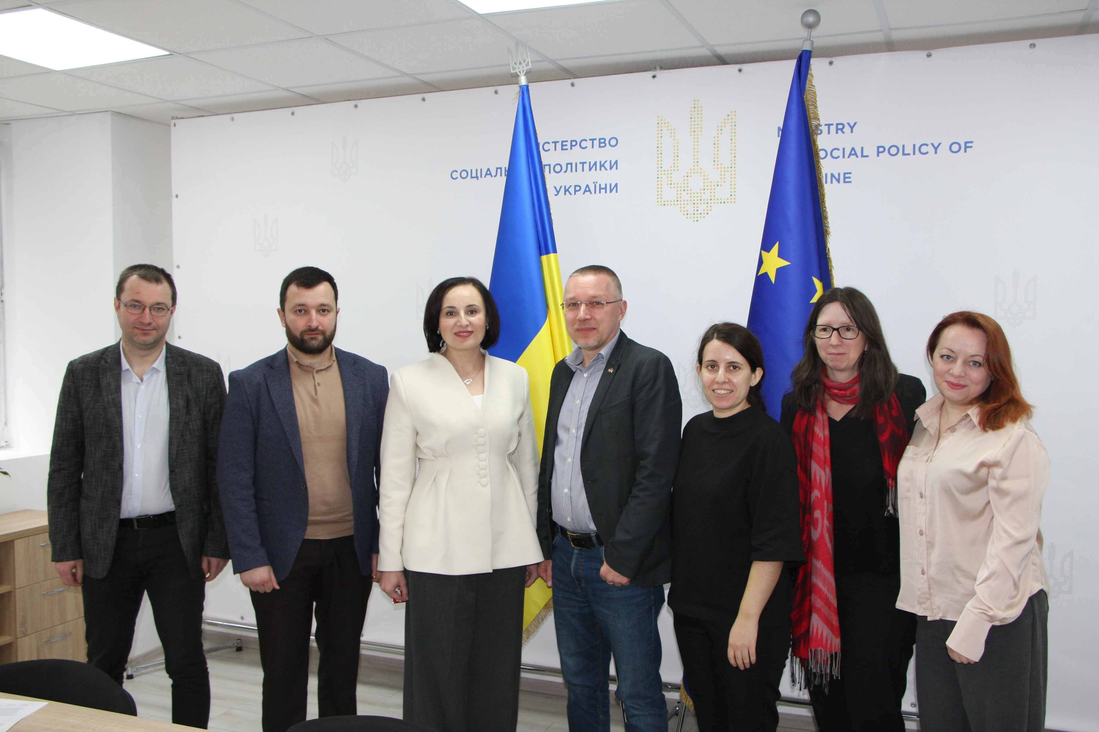 На фото зображені представники Мінсоцполітики та проєкту «Реабілітація травм для України (TRUE)»  на фоні прапорів України та ЄС