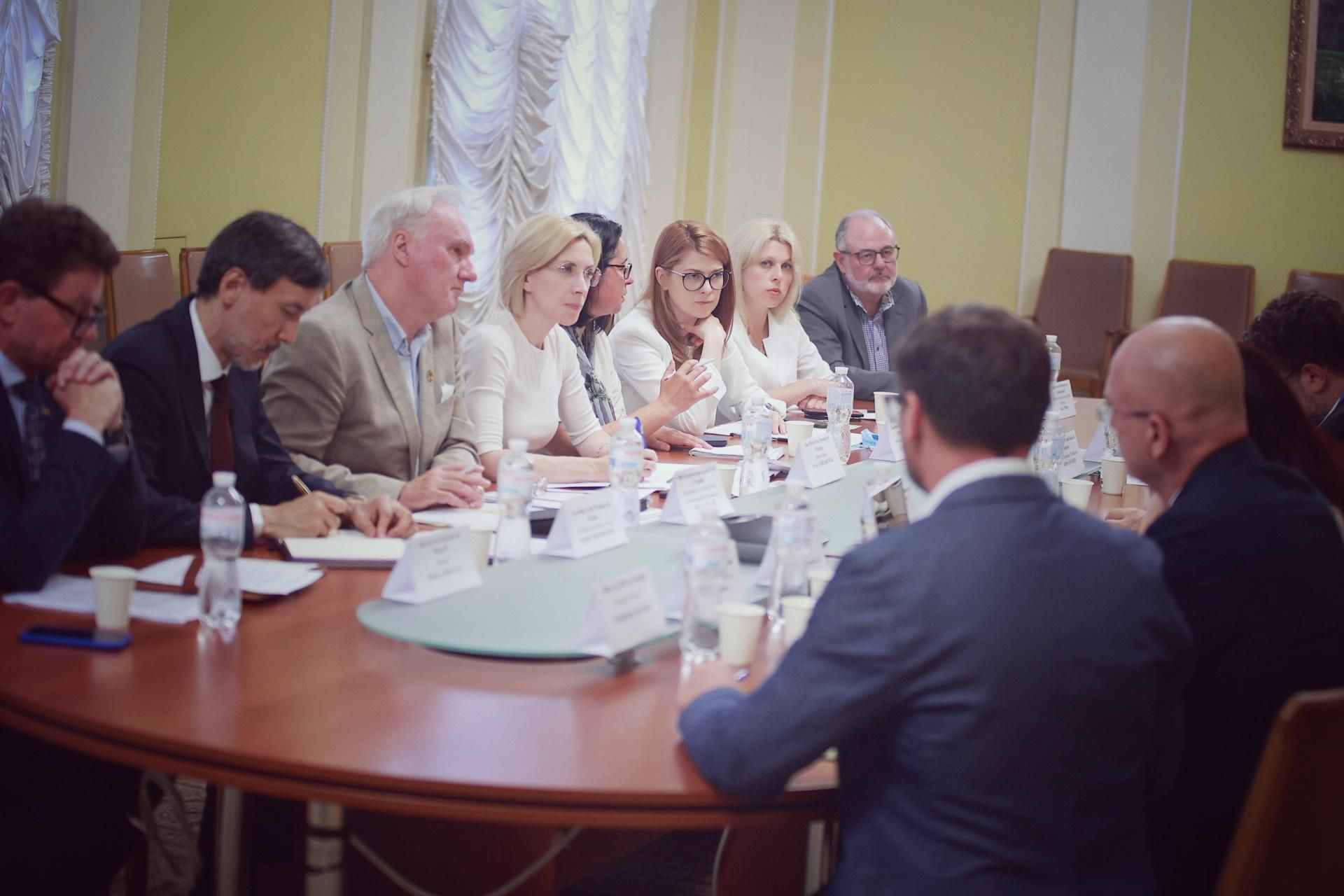 На фото чоловіки та жінки сидять за столом під час наради