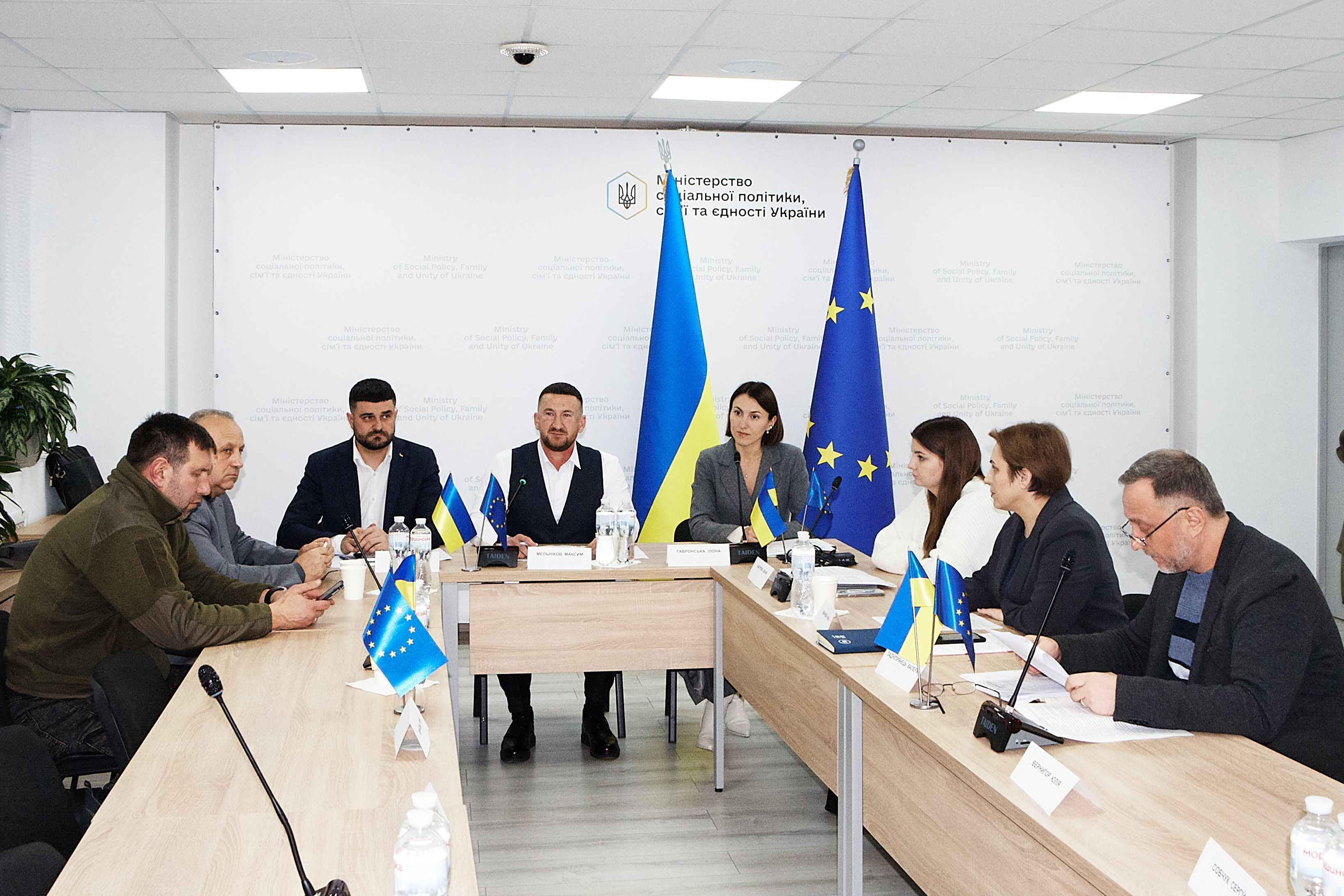 На фото чоловіки та жінки сидять за столом під час засідання Громадської ради