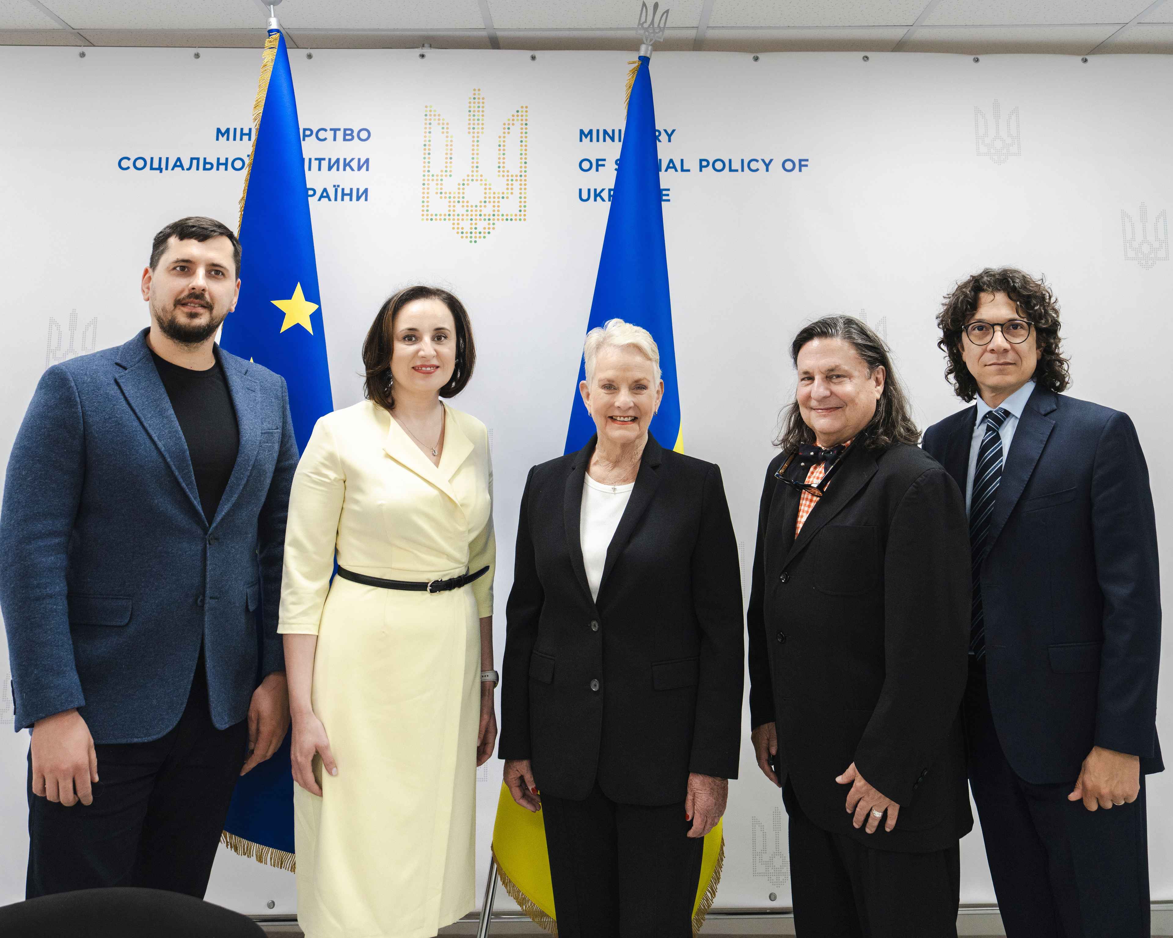 На фото чоловіки та жінки стоять на фоні прапорів України та ЄС