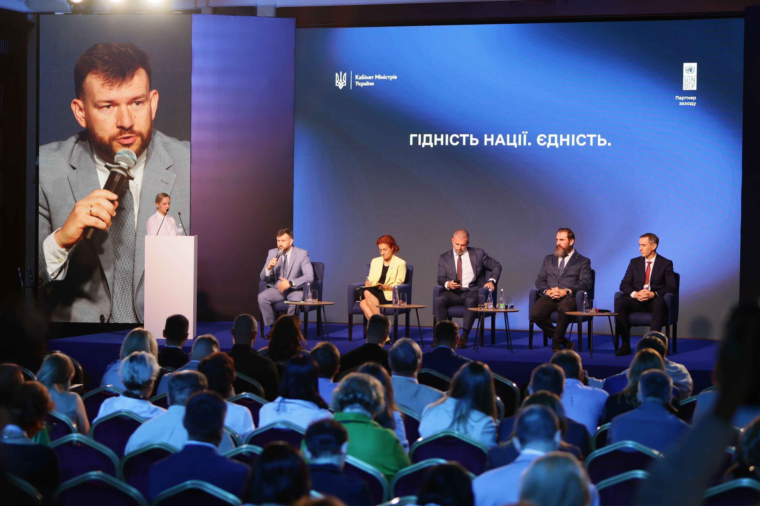 На фото чоловіки і жінки сидять у президії під час презентації Програми Уряду