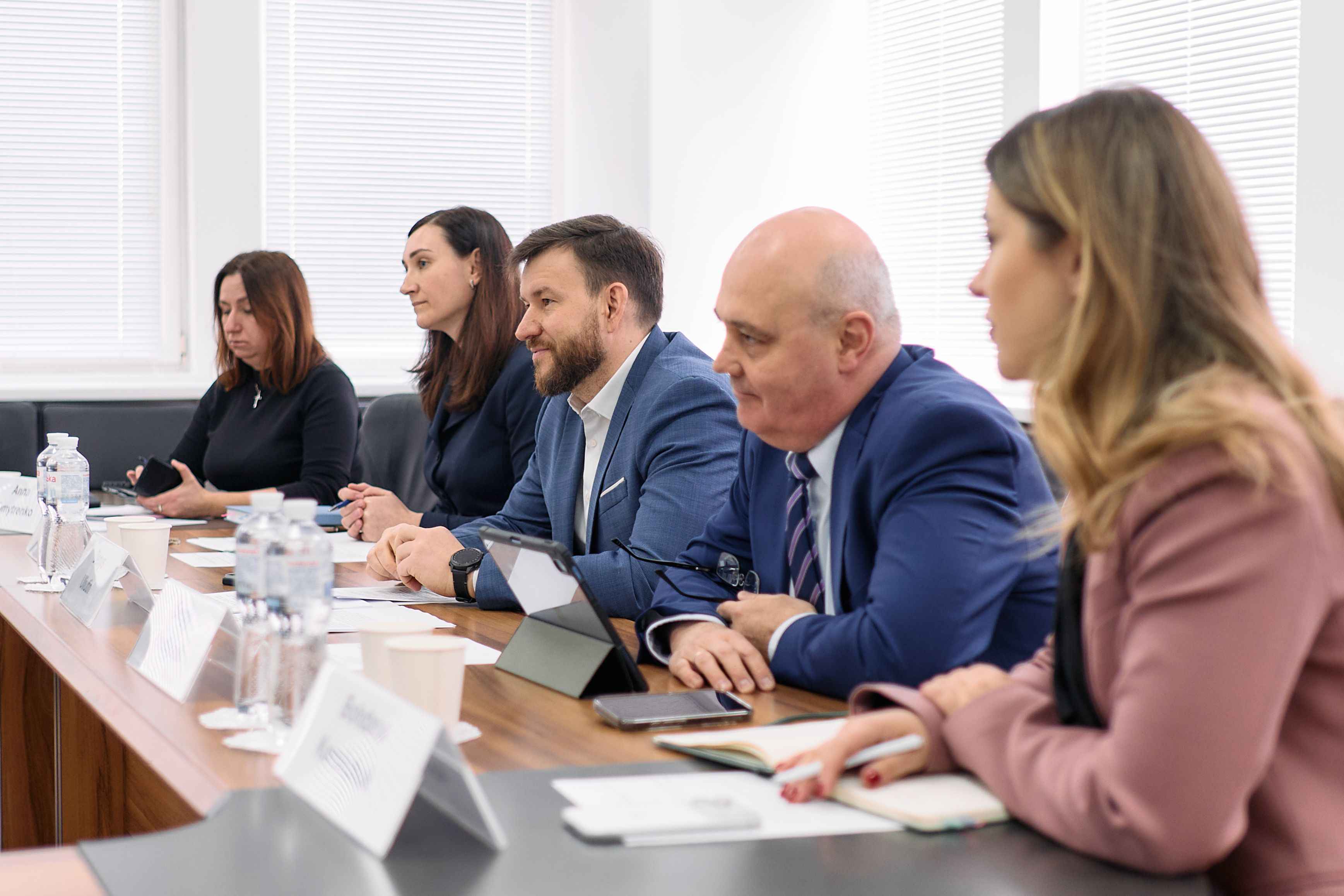 На фото чоловіки та жінки сидять за столом під час зустрічі