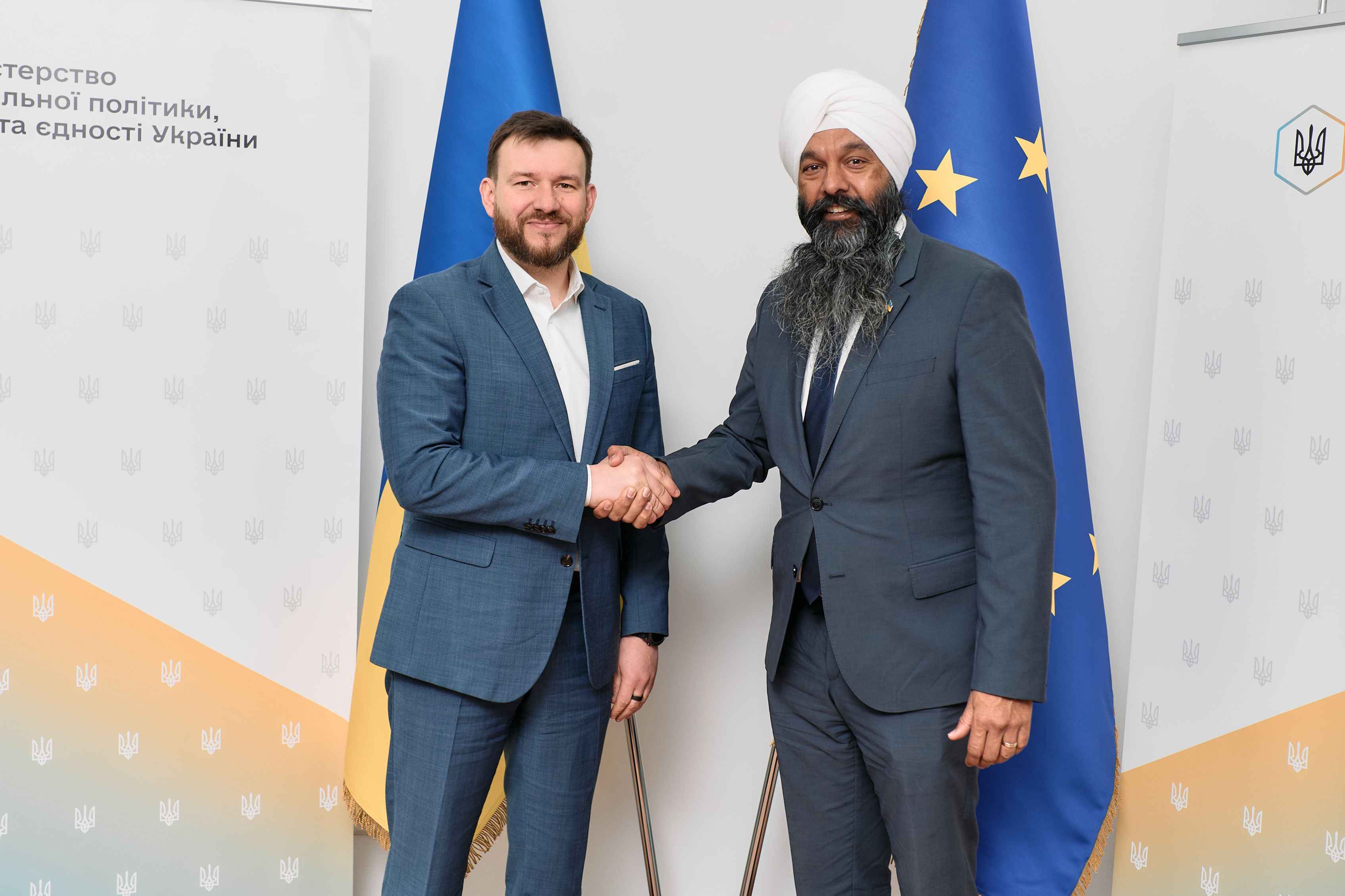 На фото чоловіки вітаються за руку на фоні прапорів України та ЄС