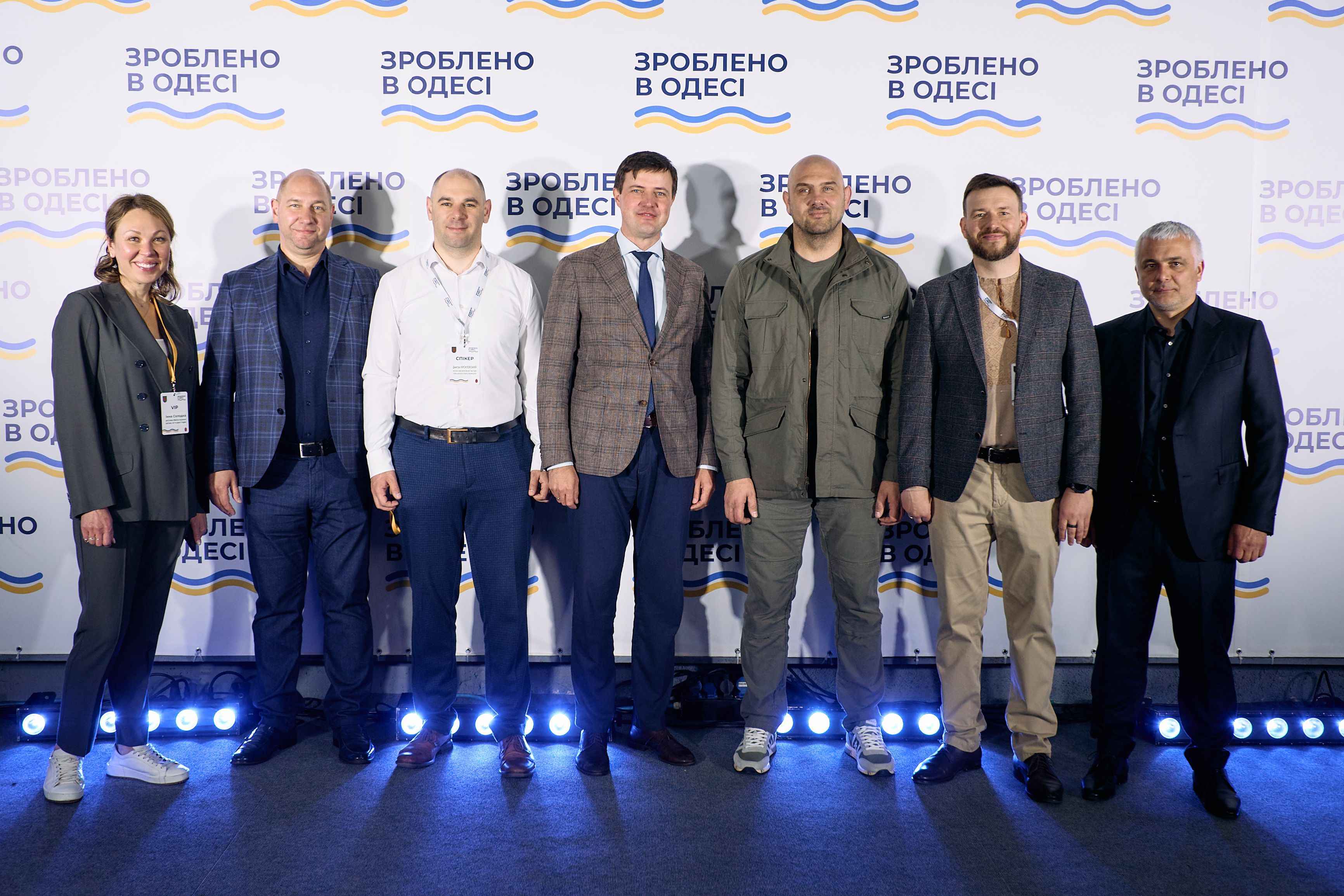 На фото жінка та чоловіки стоять на фоні банеру