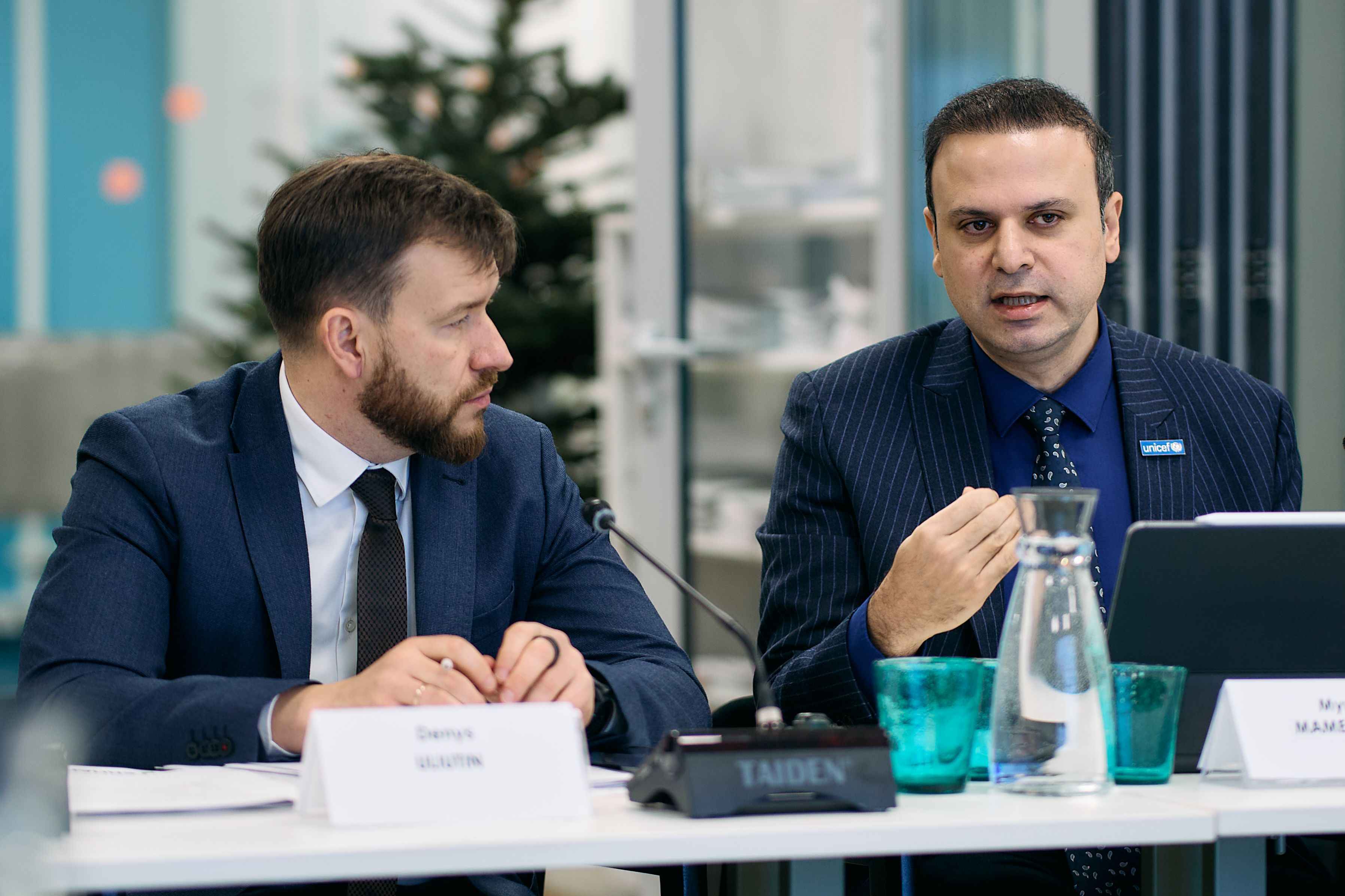 На фото чоловіки  сидять за столом під час заходу