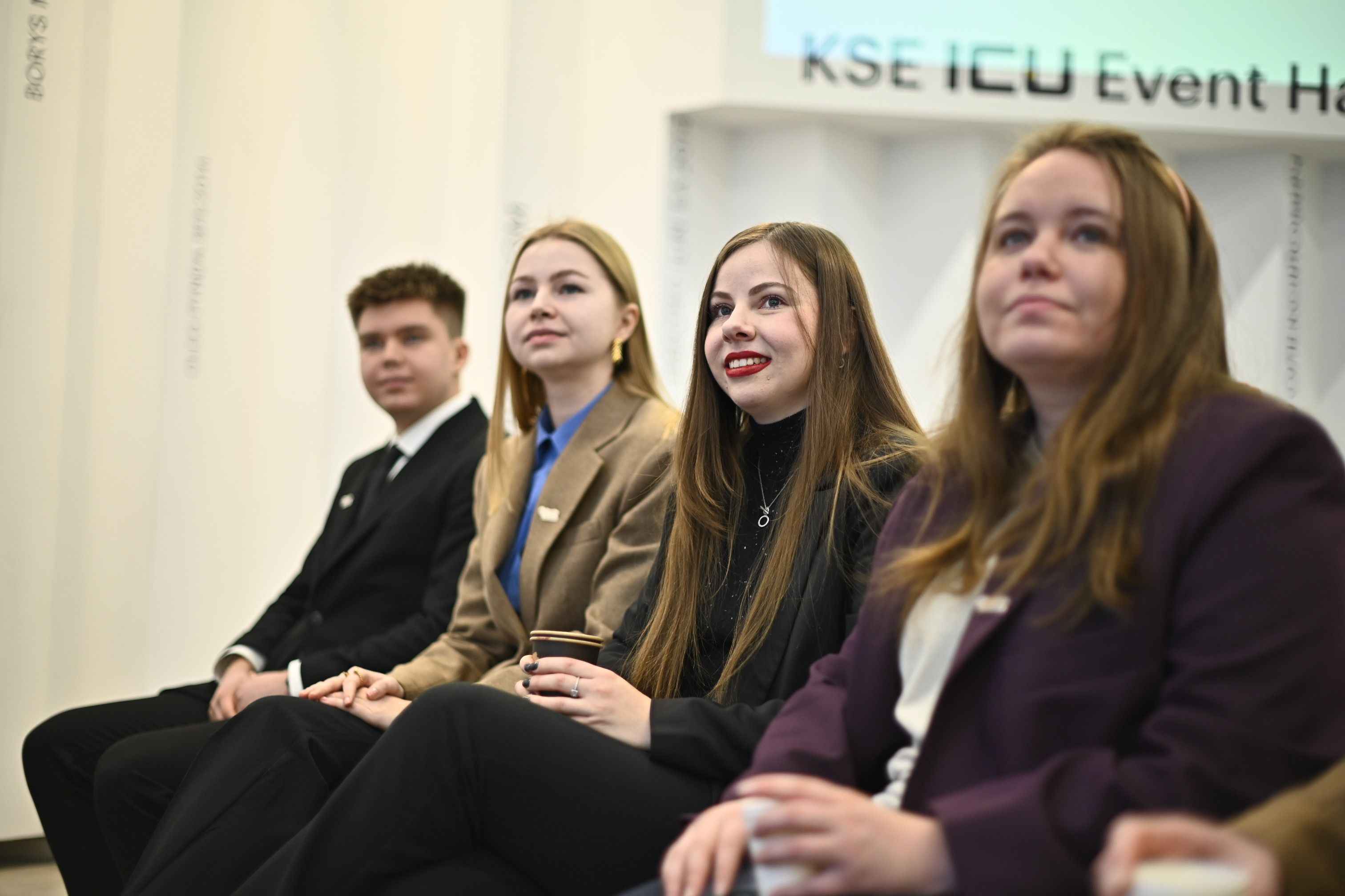 На фото хлопець та дівчата сидять в залі під час заходу