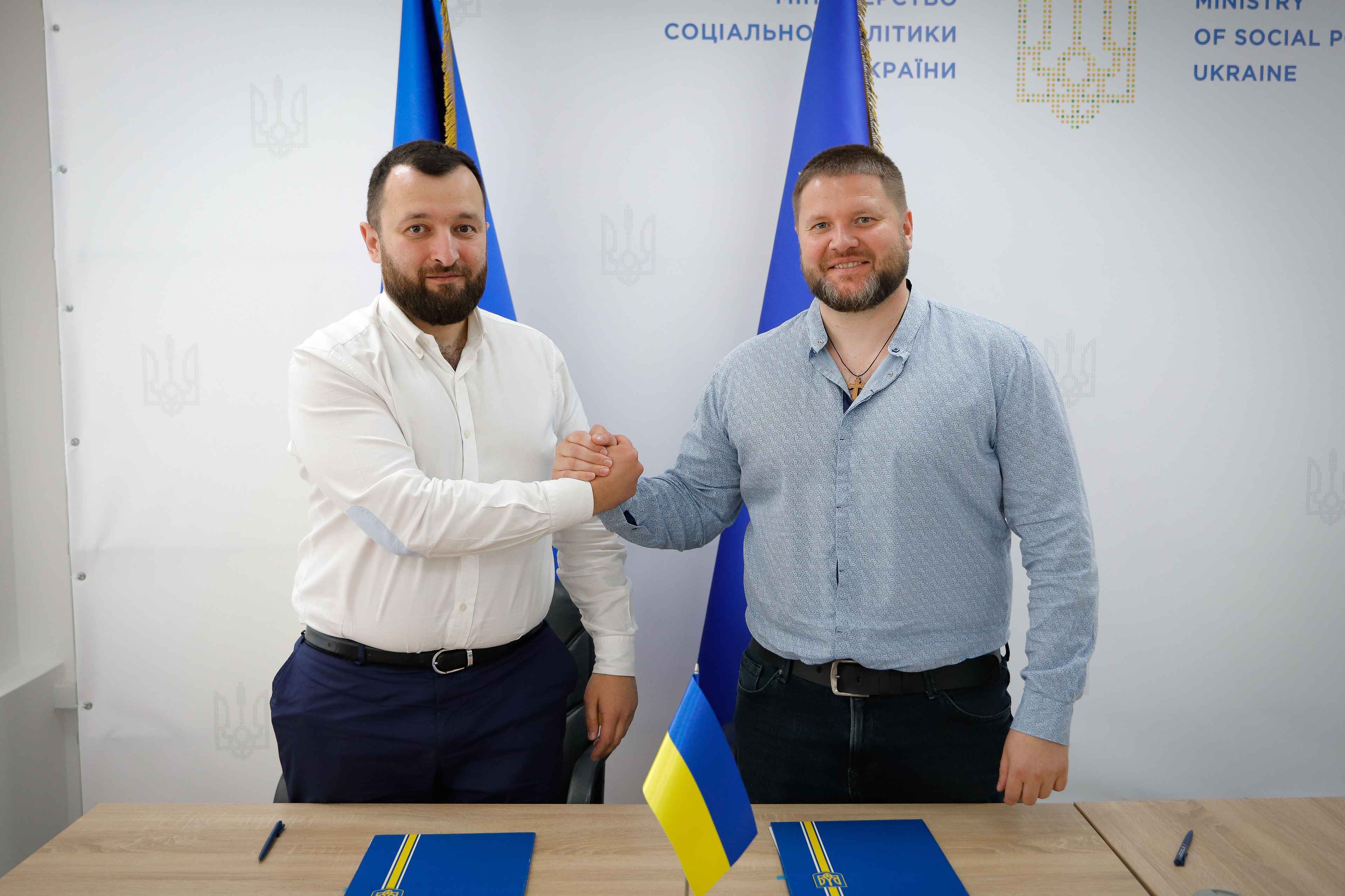 На фото два чоловіки на фоні прапорів України та ЄС