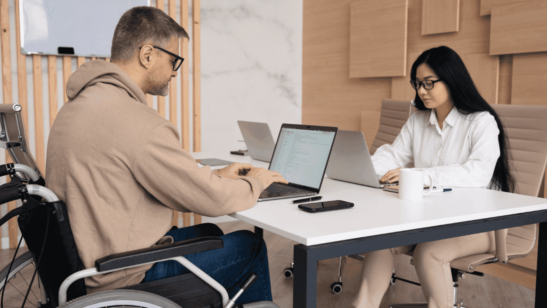 На фото чоловік з інвалідністю та жінка працюють за столом з ноутбками