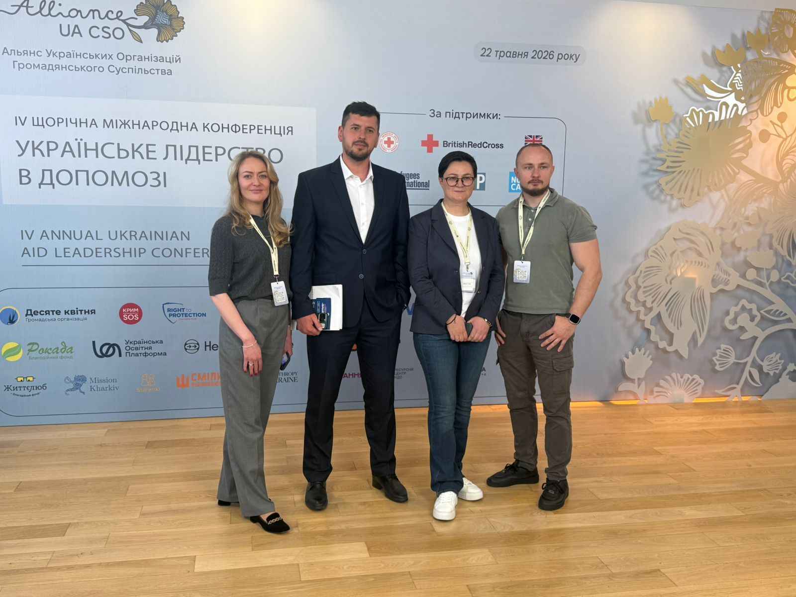 На фото чоловіки та жінки стоять на фоні банеру