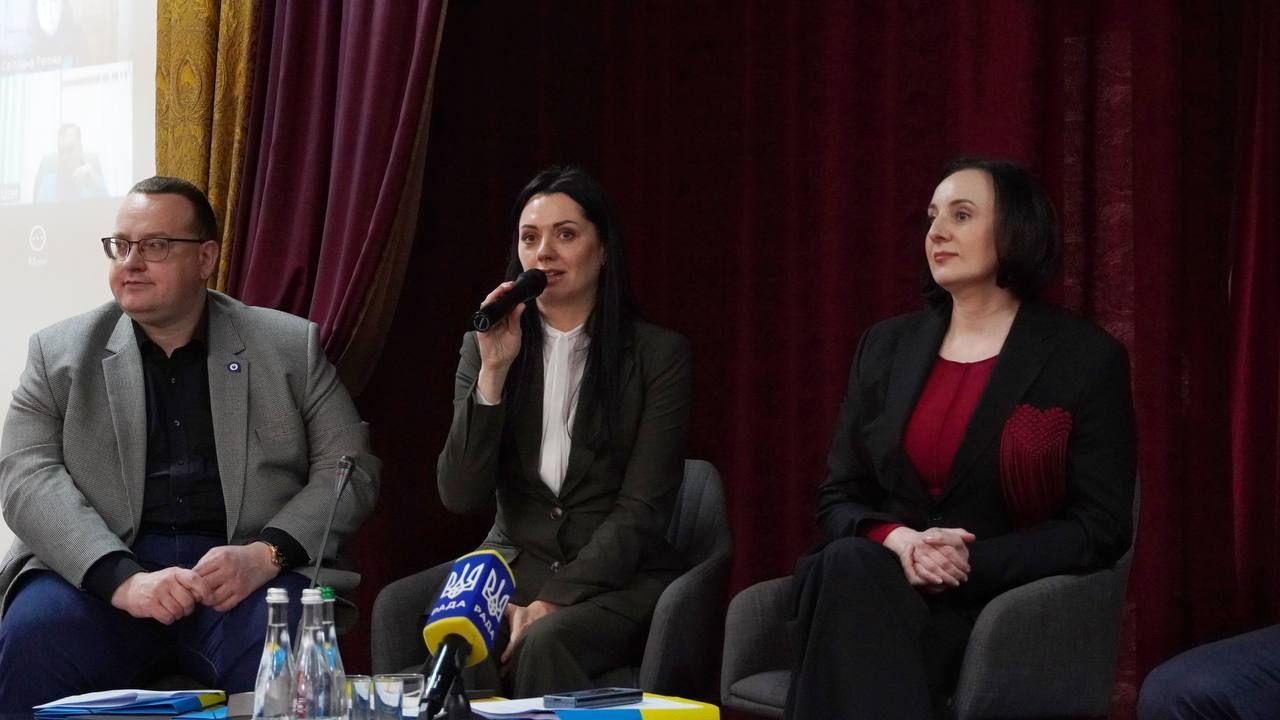 На фото зображено двох жінок і чоловіка, які сидять за столом