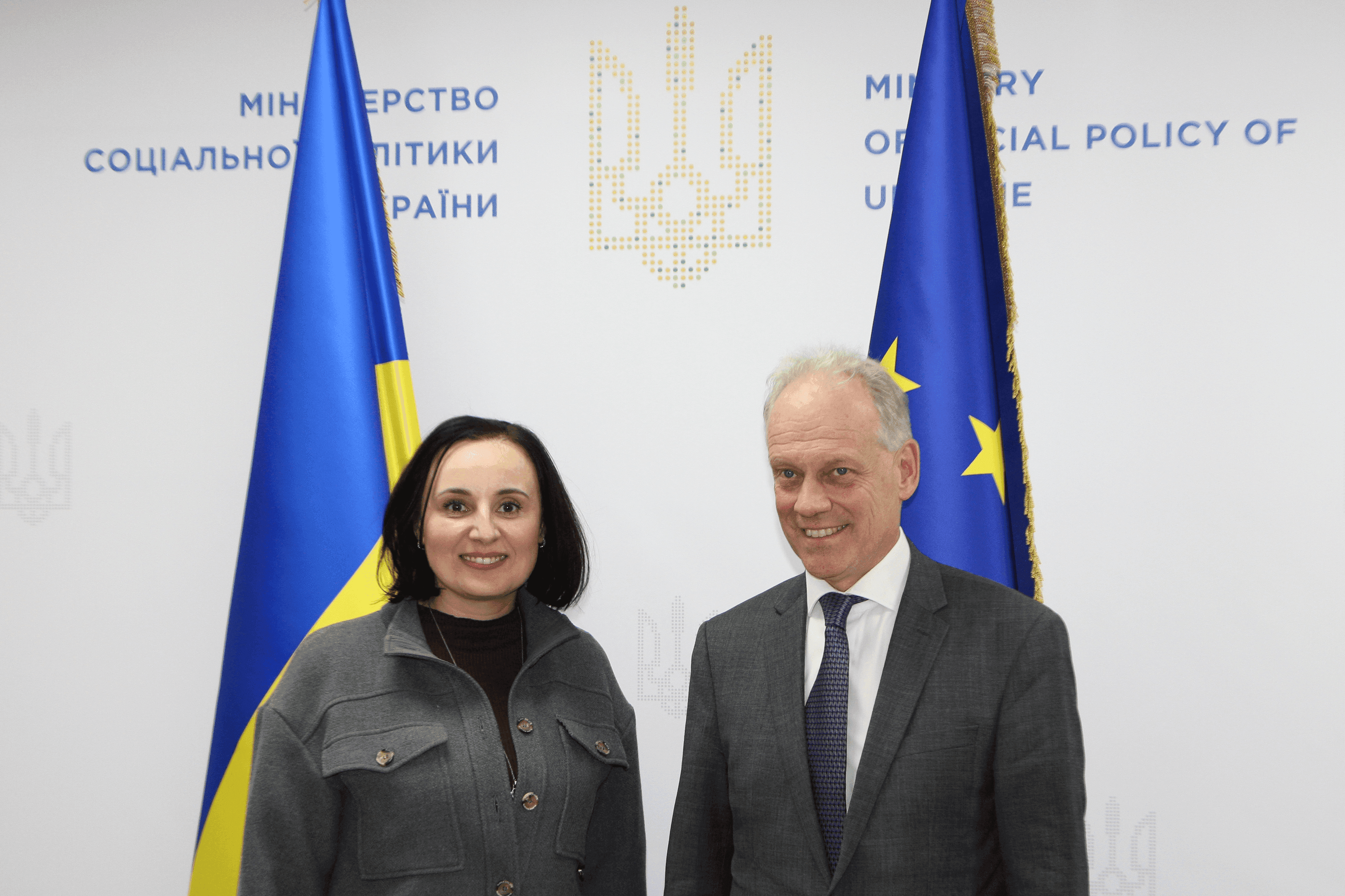 Міністр соціальної політики України Оксана Жолнович та генеральний директор Генерального директорату Європейської Комісії із питань розширення та Східного сусідства (DG ENEST) Герт Купман фотографуються на фоні прапорів України  та ЄС