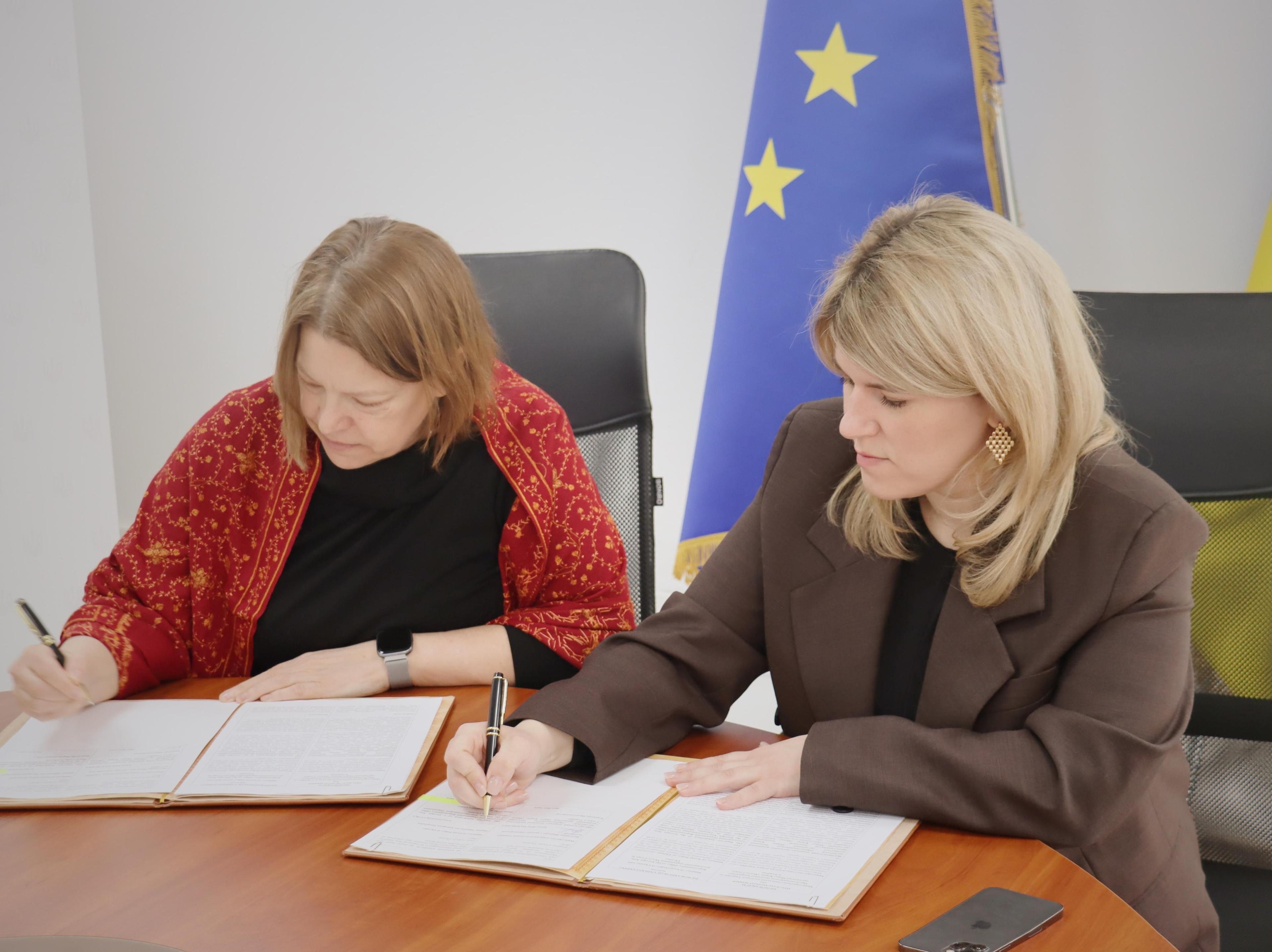 Двоє жінок на фоні прапору Європейського Союзу підписують Меморандум