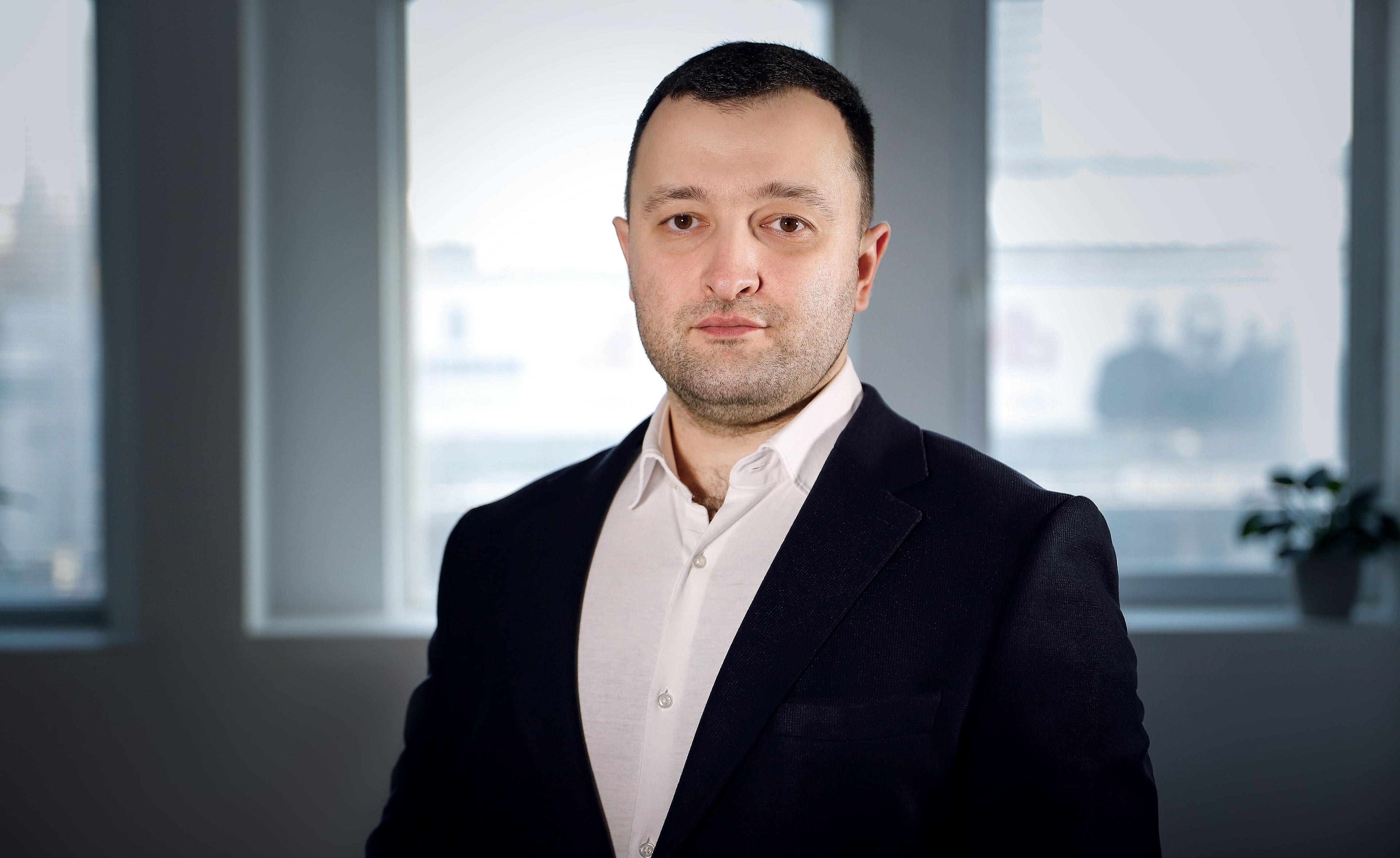 Чоловік в чорному піджаку і білій сорочці стоїть на фоні вікна. Це Василенко Володимир Андрійович, Заступник Міністра соціальної політики України