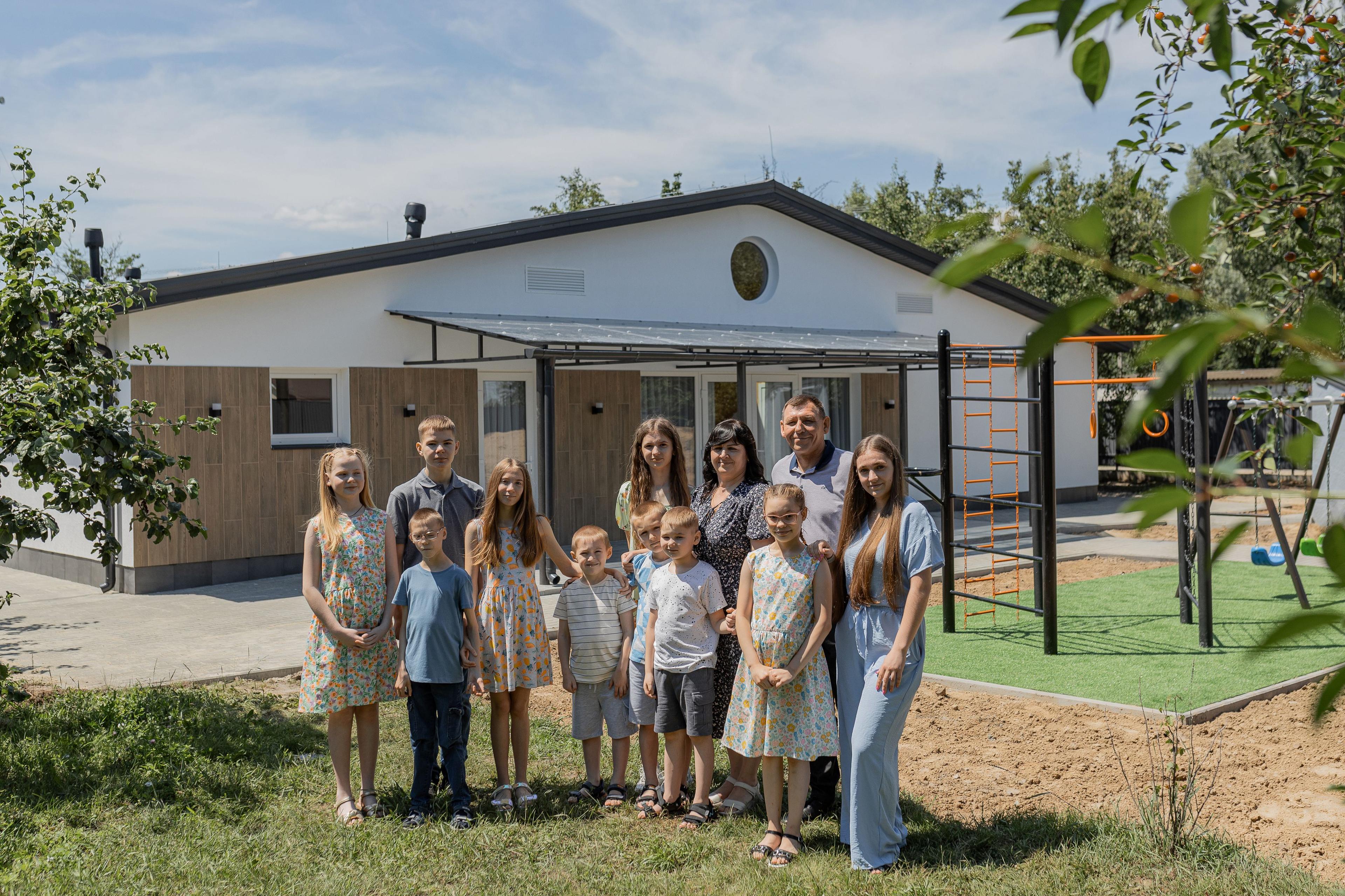 На фото зображена велика родина на фоні будинку