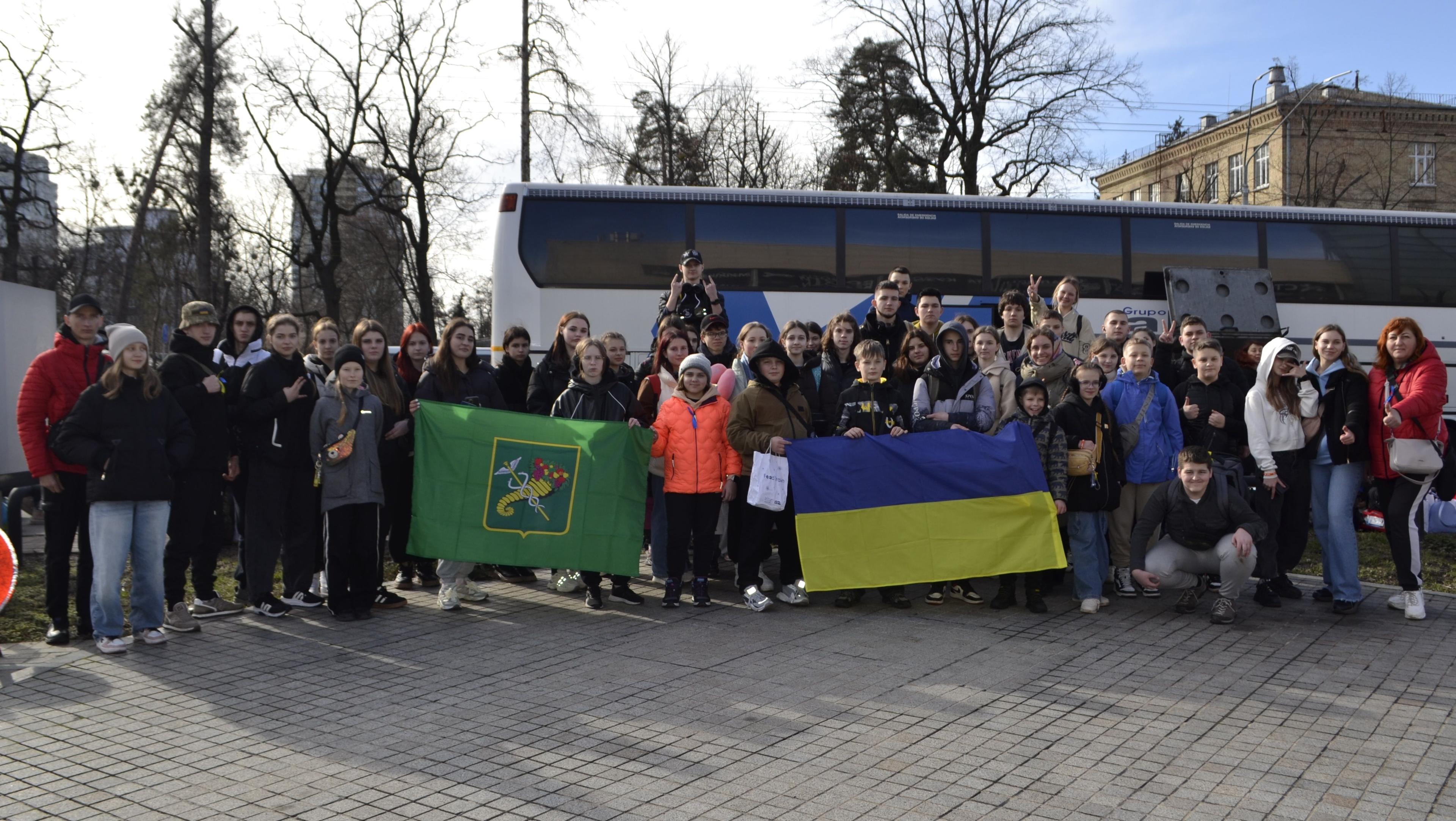 Діти з прапорами на фоні автобуса