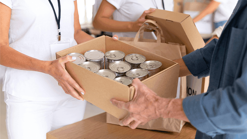 Людина передає коробку з банками продуктів іншій людині. Це зображення процесу надання гуманітарної допомоги.