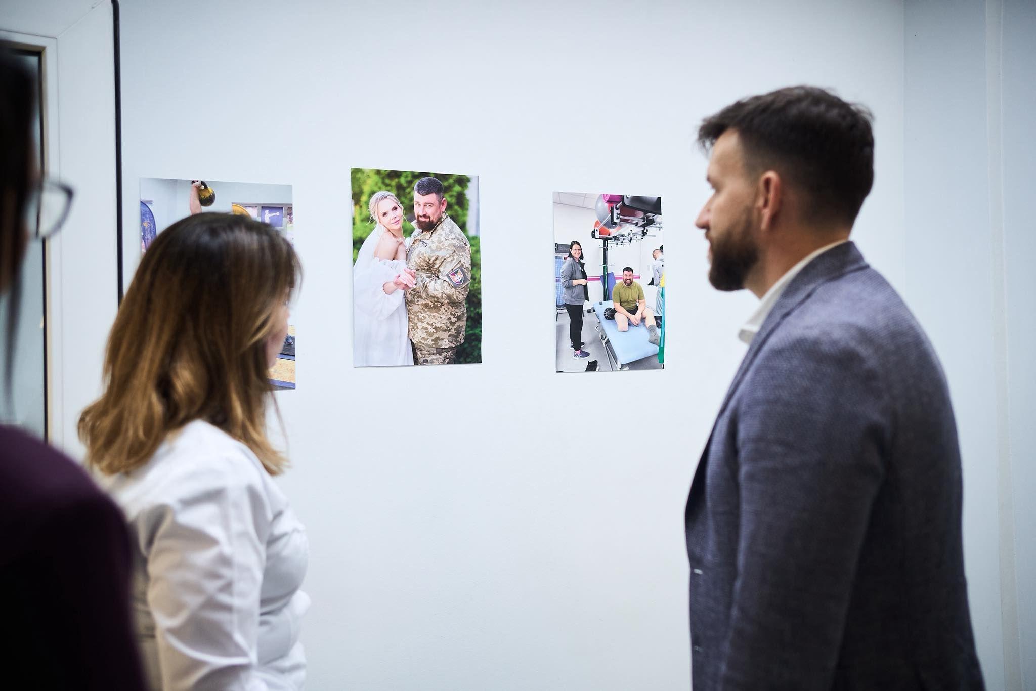 На фото жінка та чоловік розглядають фотографії, що висять на стіні