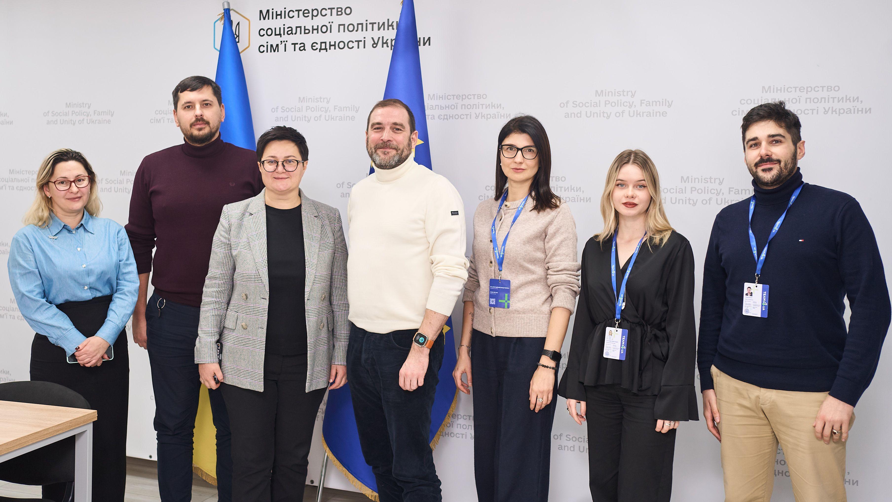 На фото чоловіки та жінка стоять на фоні прапорів України та ЄС