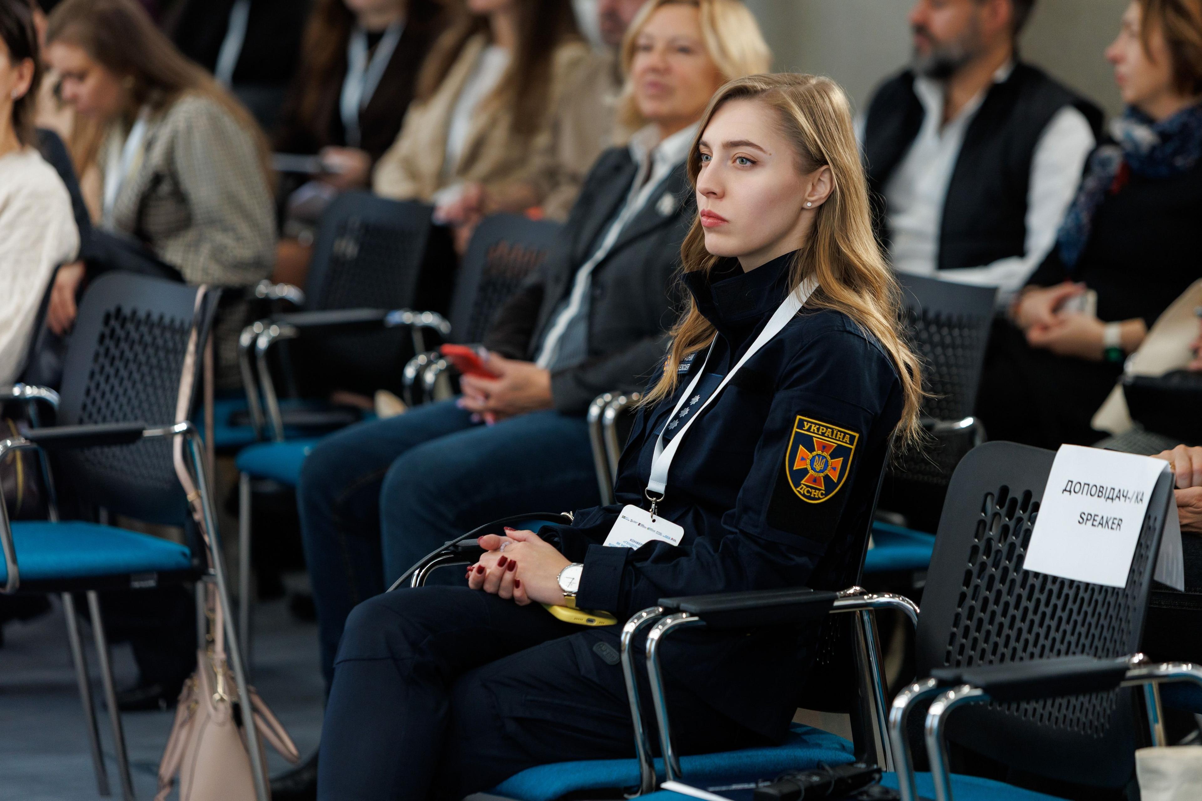 На фото жінки та чоловіки сидять у залі під час заходу