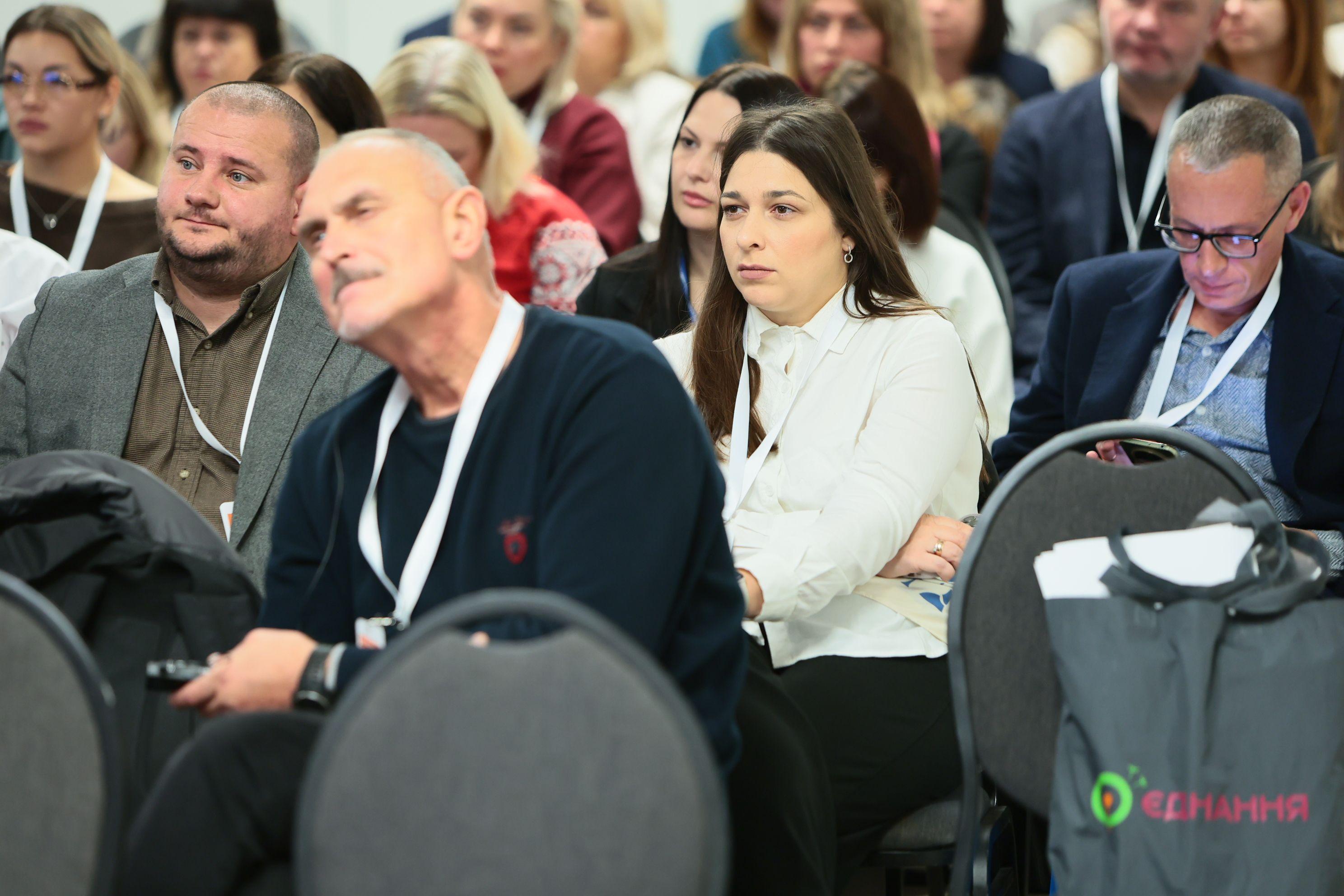 На фото чоловіки та жінки сидять у залі під час заходу