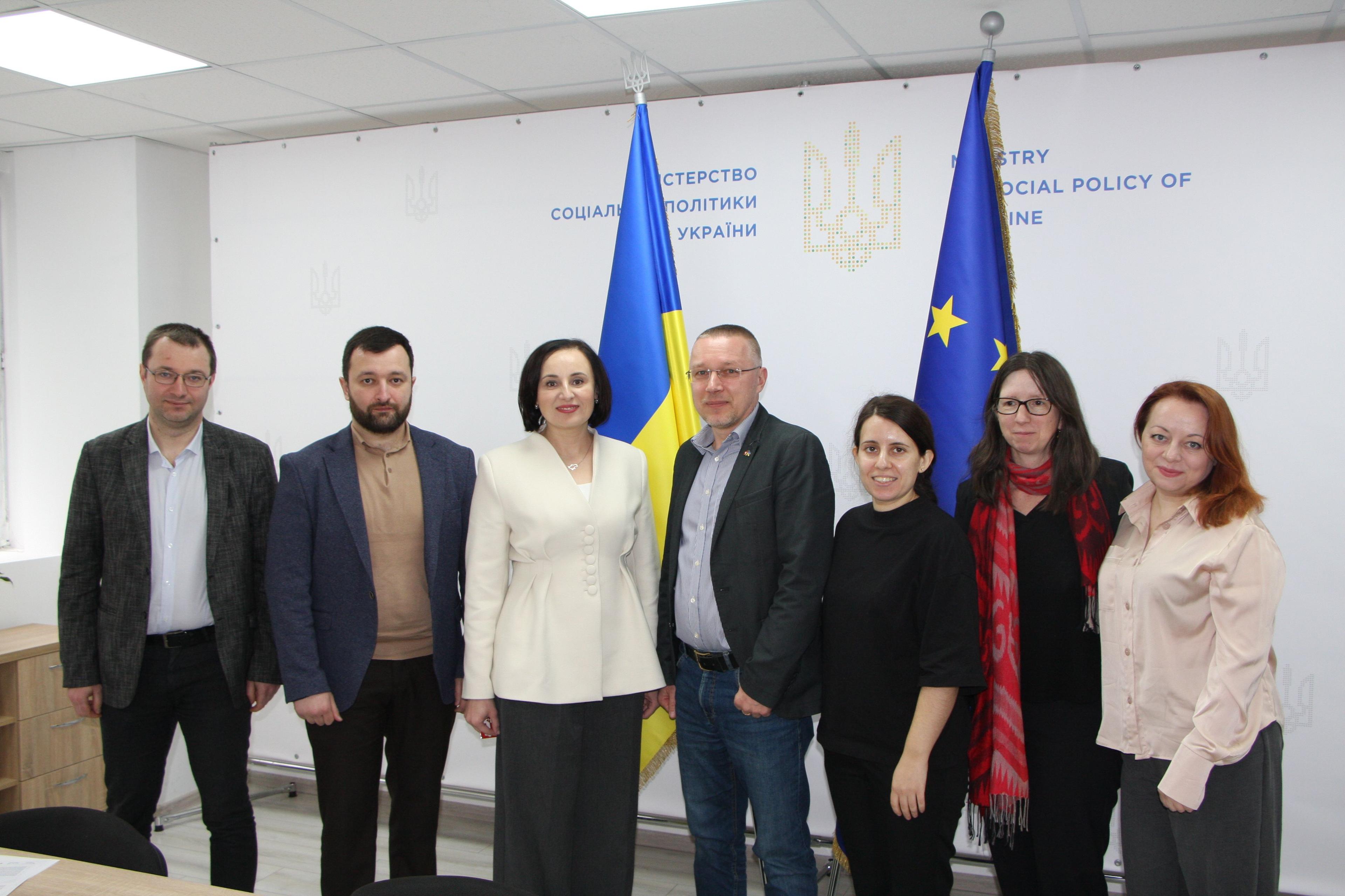 На фото зображені представники Мінсоцполітики та проєкту «Реабілітація травм для України (TRUE)»  на фоні прапорів України та ЄС