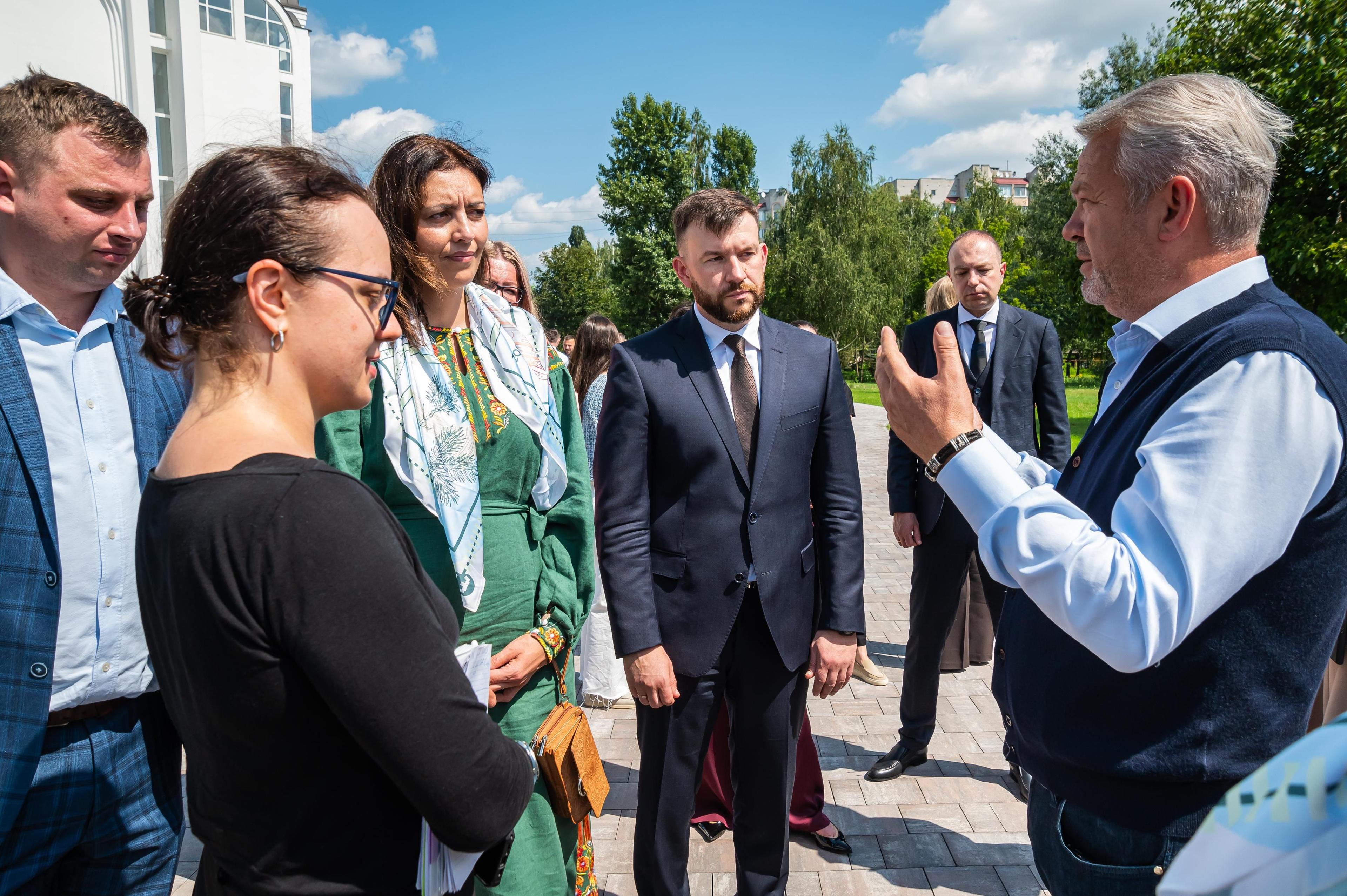 На фото чолвіки та жінки стоять на вулиці і щось обговорюють