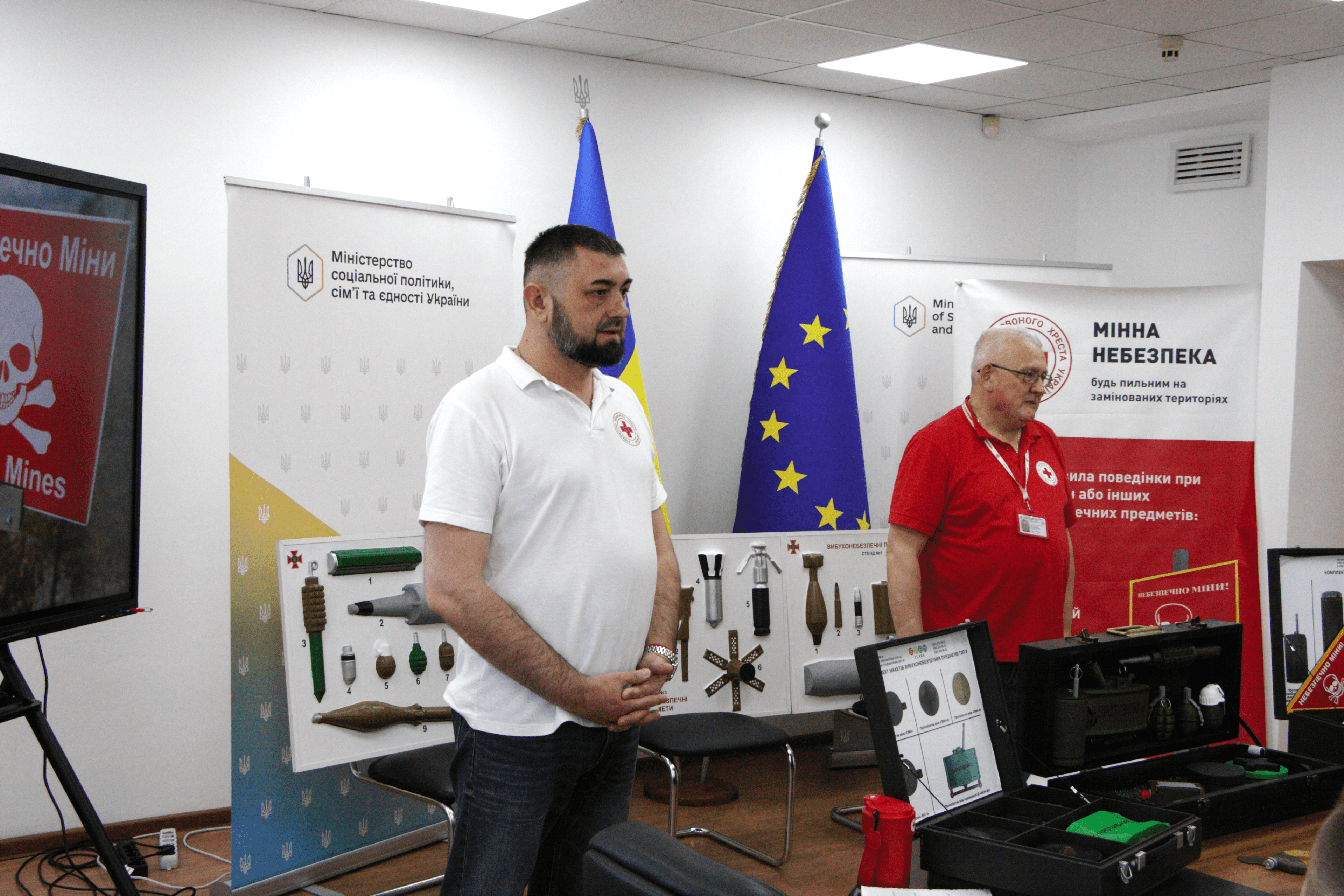 На фото чоловіки розповідають у приміщенні про мінну безпеку