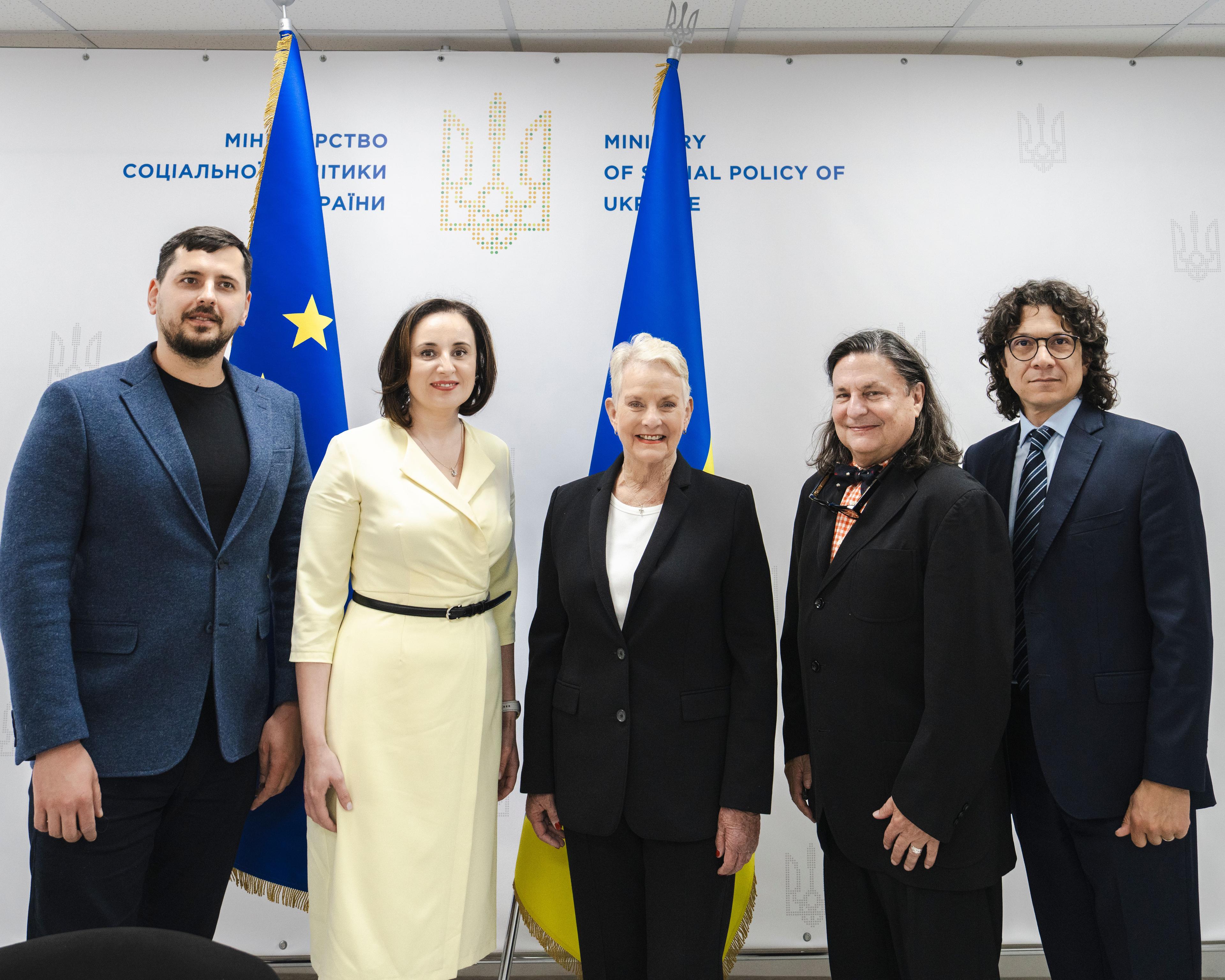 На фото чоловіки та жінки стоять на фоні прапорів України та ЄС