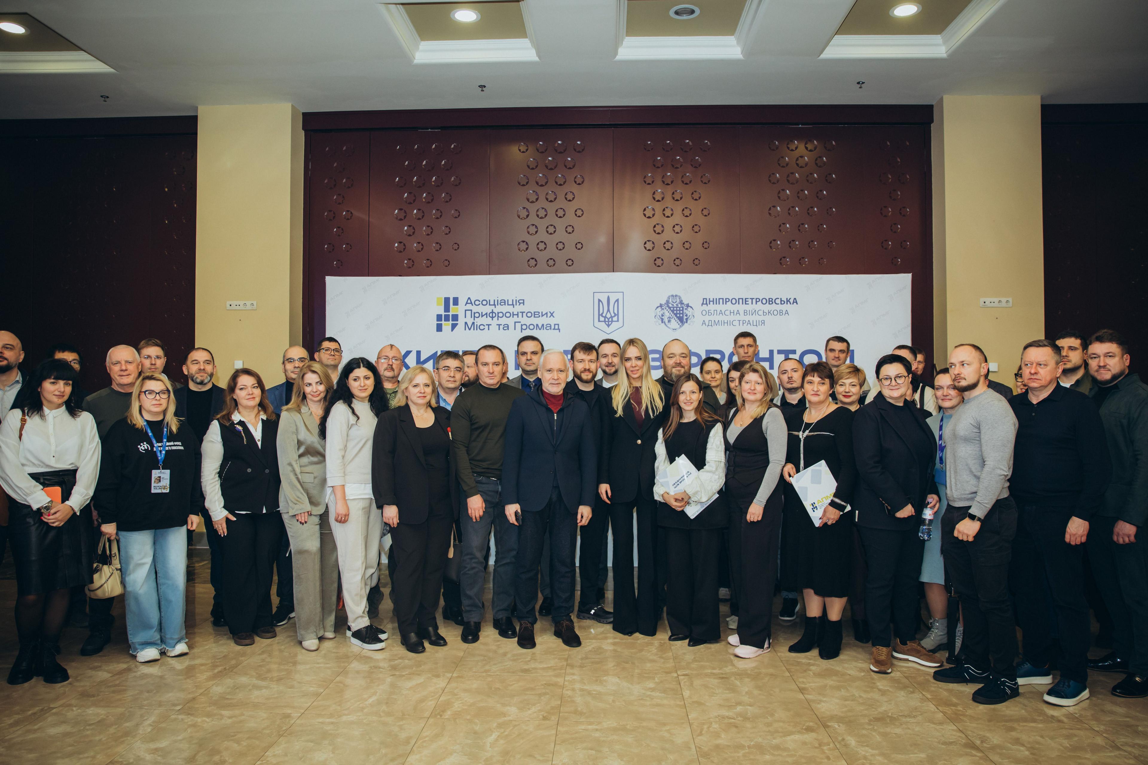 На фото жінки та чоловіки стоять на фоні банеру після заходу