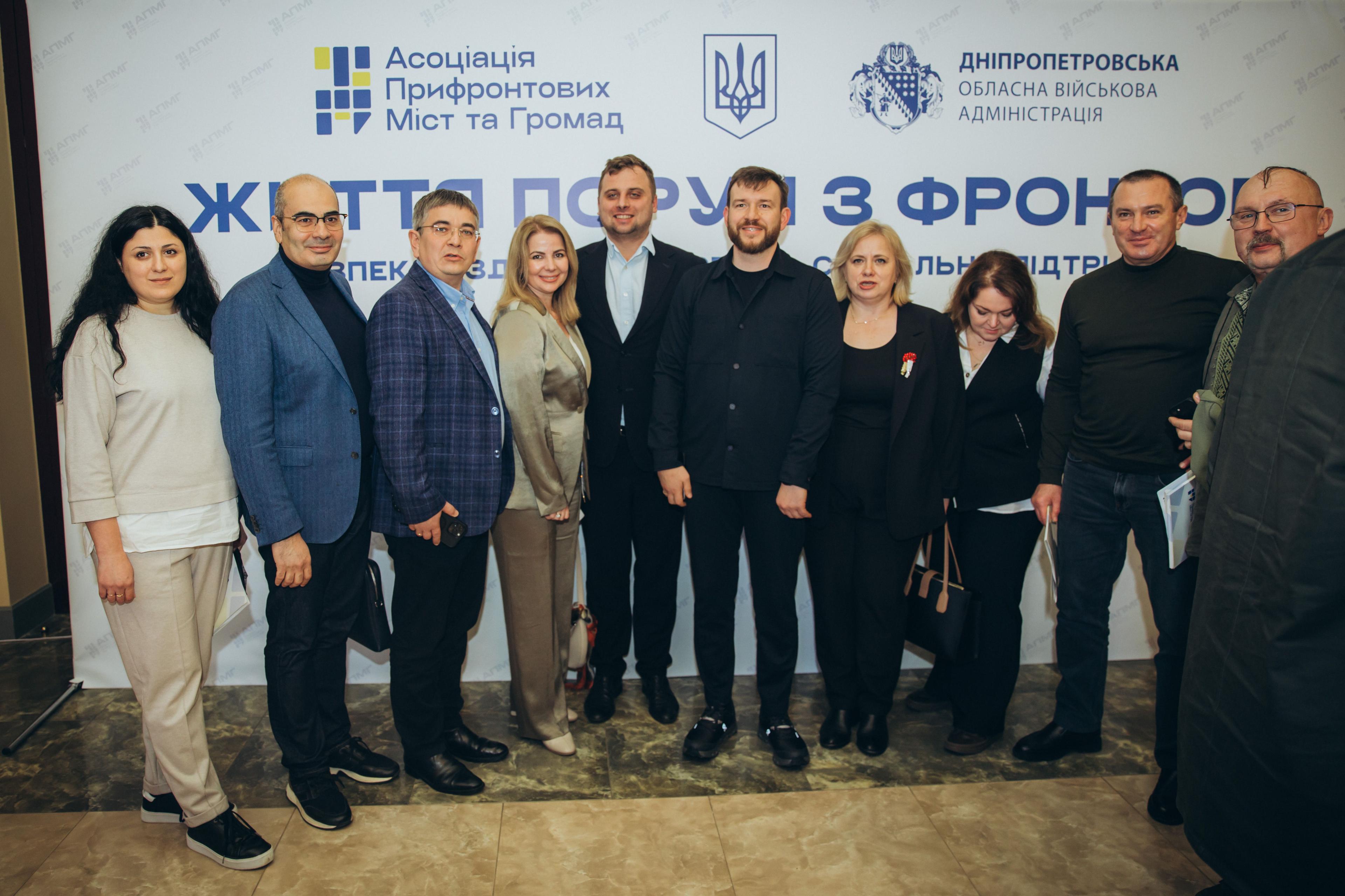 На фото чоловіки та жінки стоять на фоні банеру після заходу