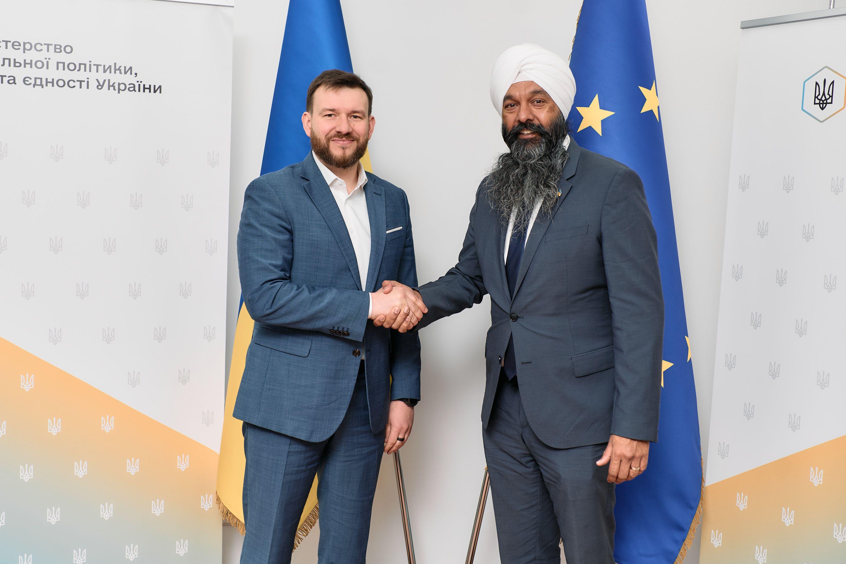 На фото чоловіки вітаються за руку на фоні прапорів України та ЄС