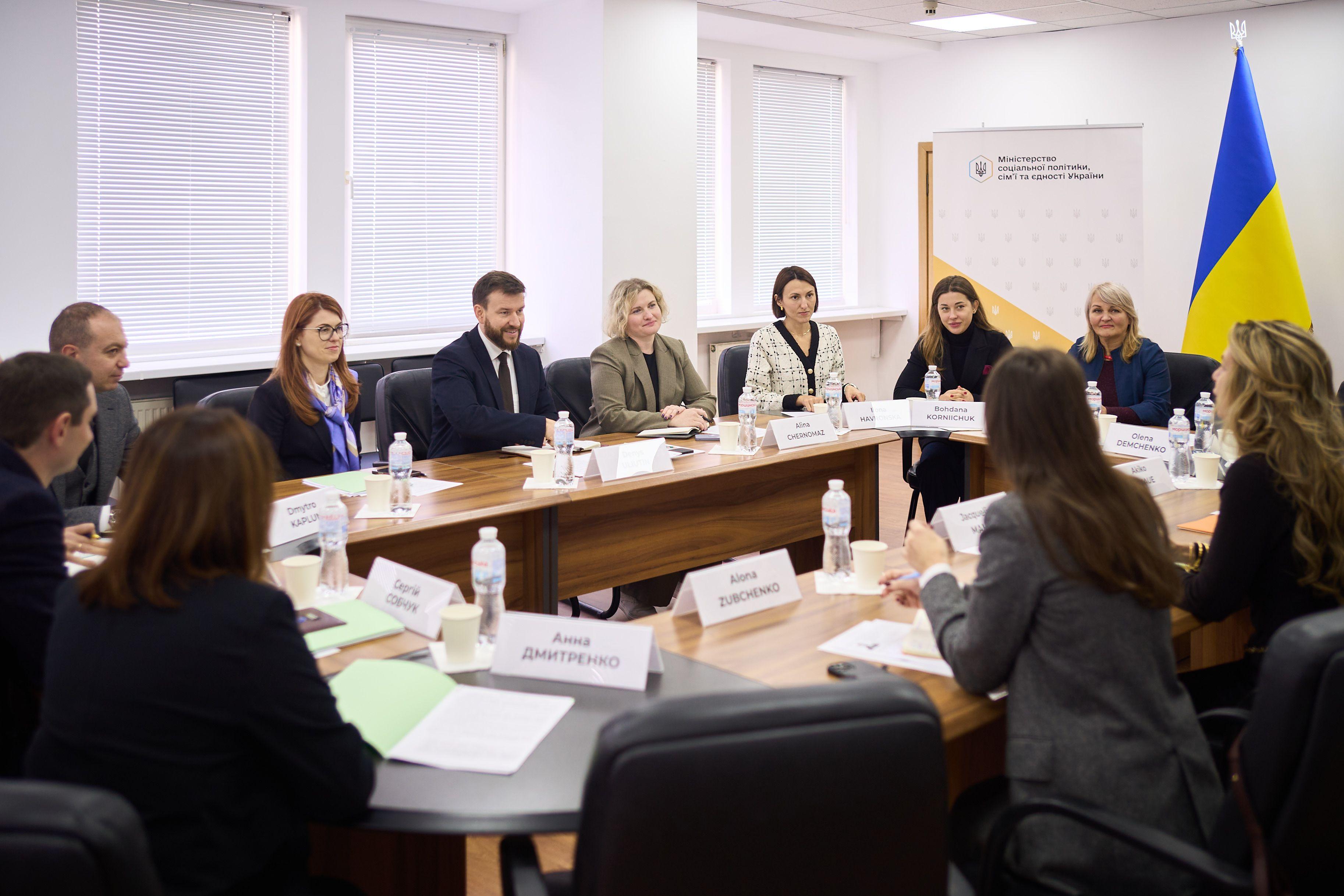 На фото чоловіки та жінки сидять за столом під час зустрічі