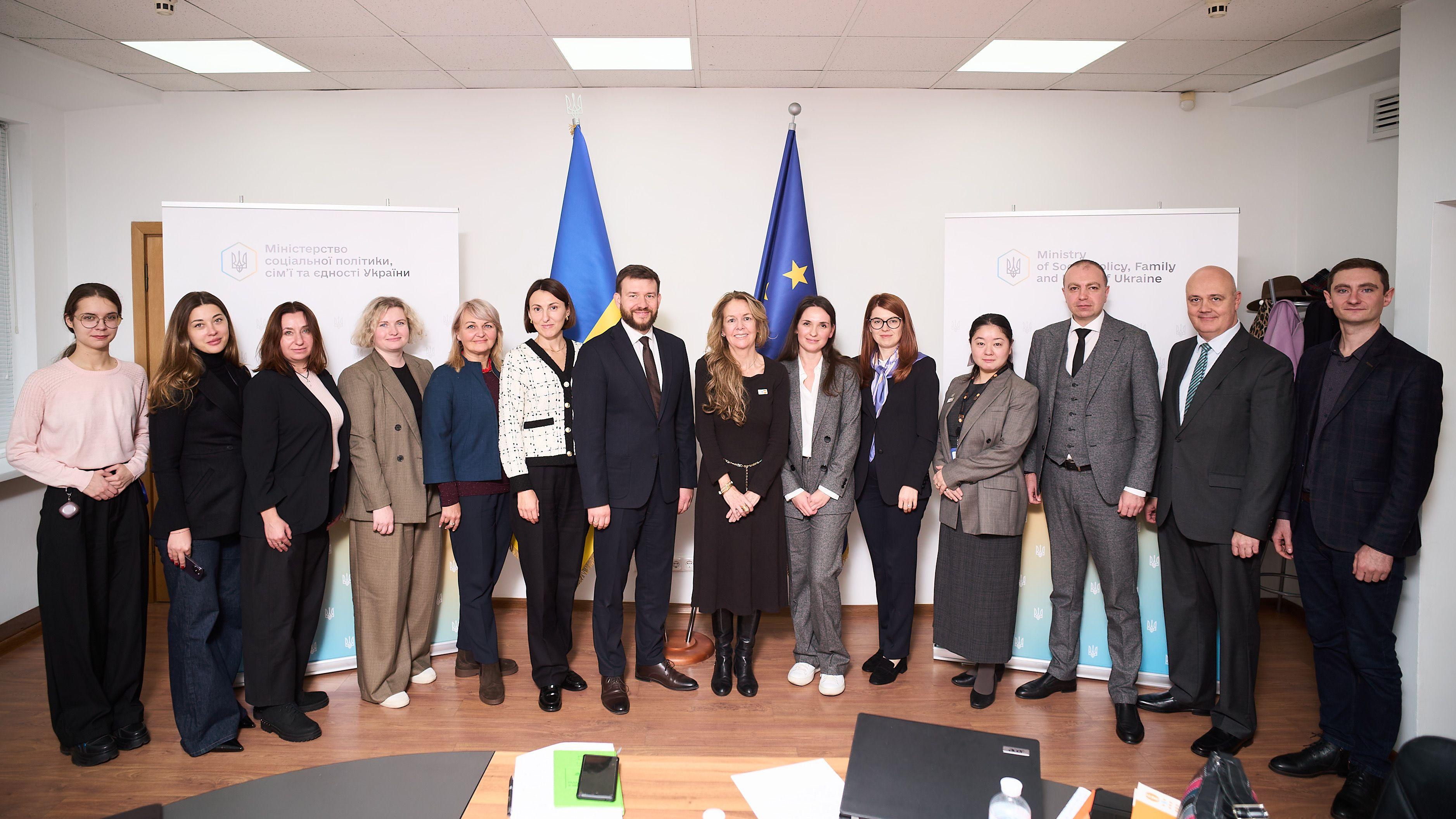 На фото чоловіки та жінки стоять на фоні прапорів України та ЄС