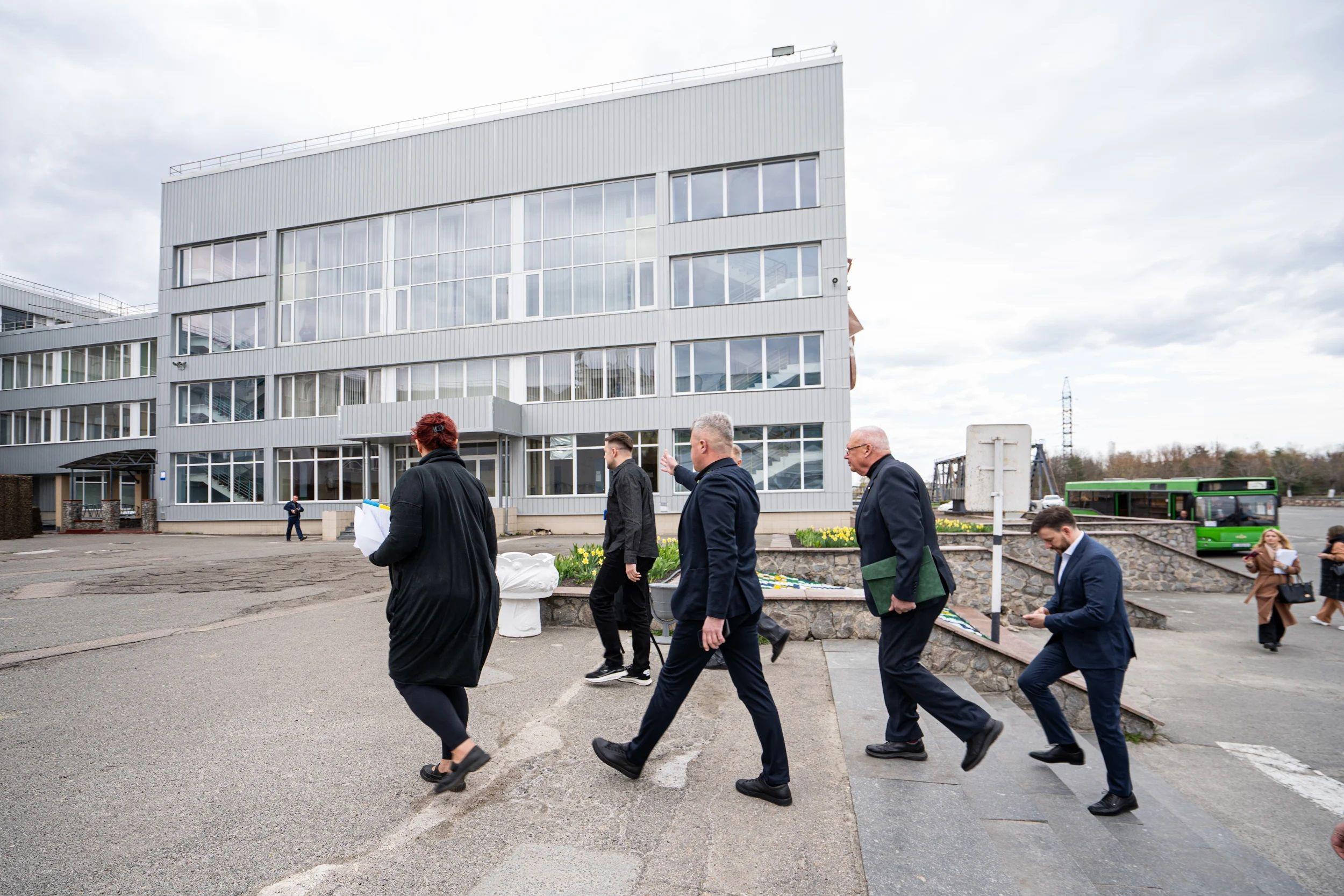 На фото жінка та чоловіки йдуть до приміщення